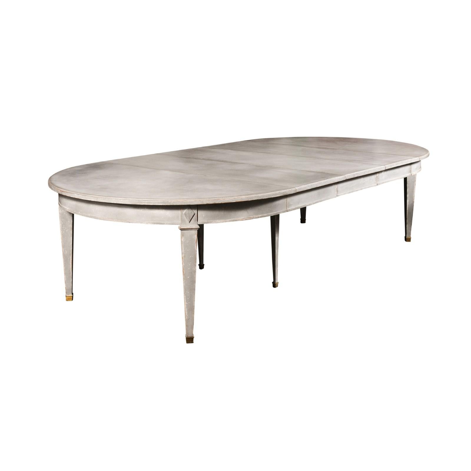 A Swedish Gustavian style painted wood extension dining room table from the early 20th century, with three leaves. Created in Sweden during the early years of the 20th century, this Swedish dining room table features an oval top resting on an apron