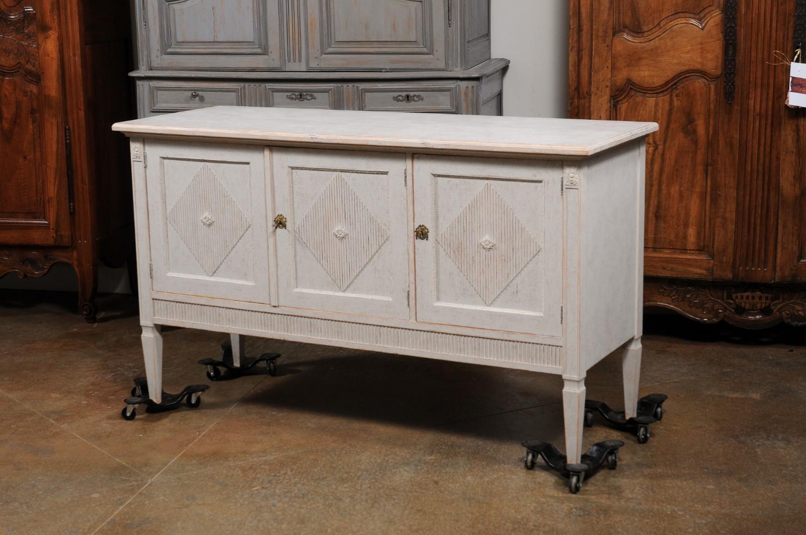 A Swedish Gustavian style painted wood sideboard from the early 20th century, with three doors and fluted diamond motifs. Created in Sweden during the early years of the 20th century, this painted sideboard features a rectangular top sitting above