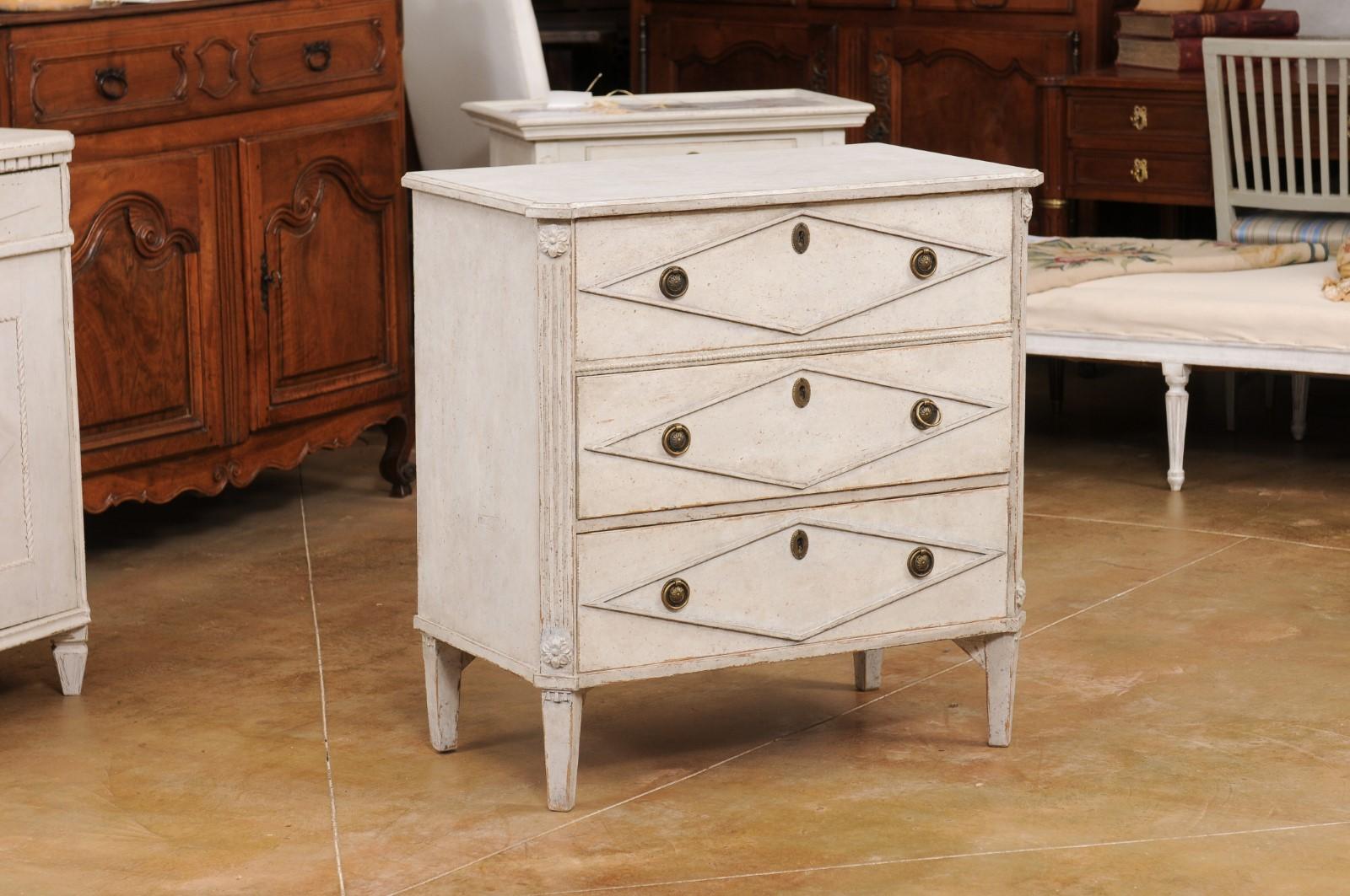 A Swedish Gustavian style painted wood chest from the early 20th century with three drawers, carved diamond motifs, fluted side posts, carved rosettes and tapered feet. Created in Sweden during the early years of the 20th century, this painted wood