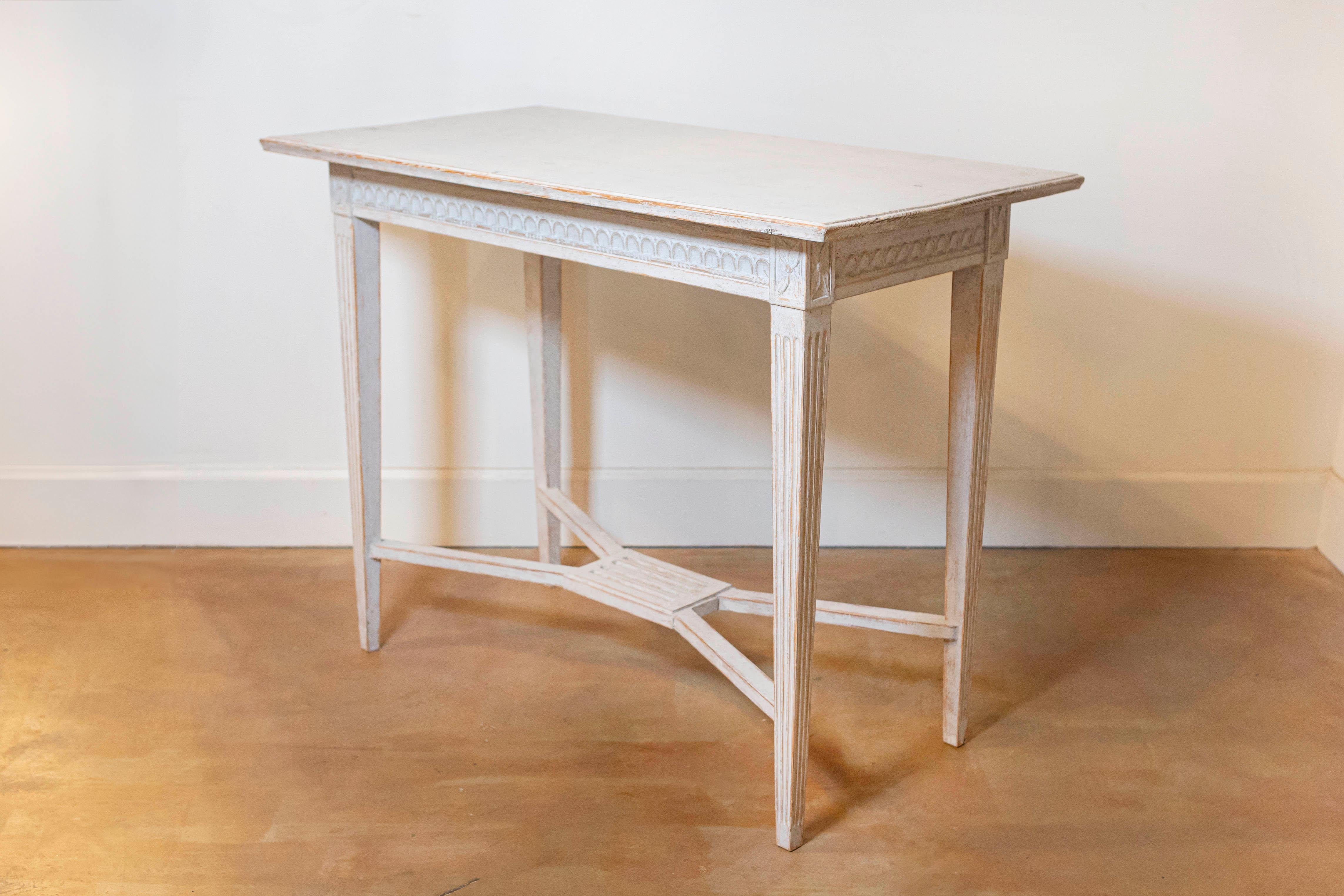 A Swedish Gustavian style painted wood console table from the early 20th century, with carved frieze, rosettes, fluted legs and X-Form cross stretcher. Created in Sweden at the Turn of the Century which saw the transition between the 19th to the