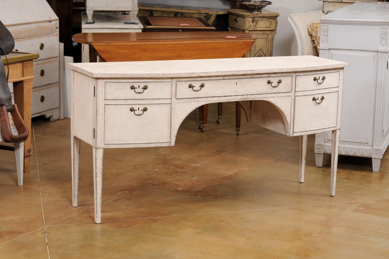 A Swedish Gustavian style bow front painted wood sideboard or desk from the early 20th century, with single drawer, two doors and tapered legs. Created in Sweden during the Turn of the Century which saw the transition between the 19th to the 20th,