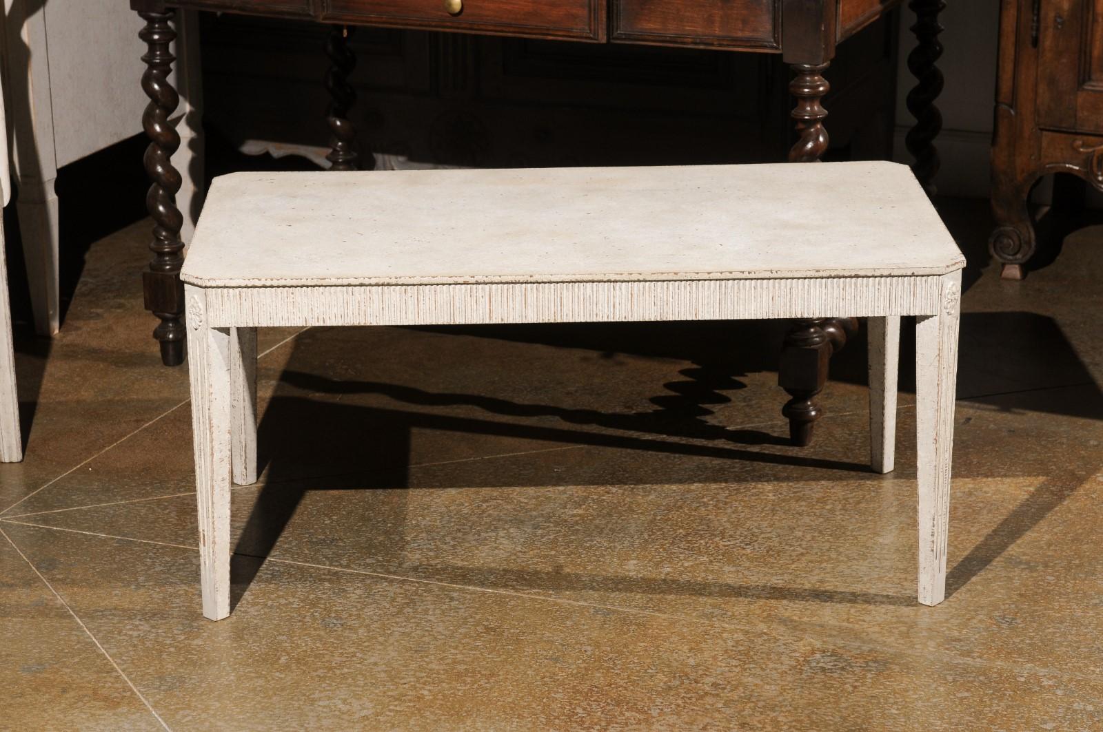 A Swedish Gustavian style painted wood coffee table from the early 20th century, with reeded apron, fluted legs and carved rosettes. Created in Sweden during the first quarter of the 20th century, this Gustavian style coffee table features a