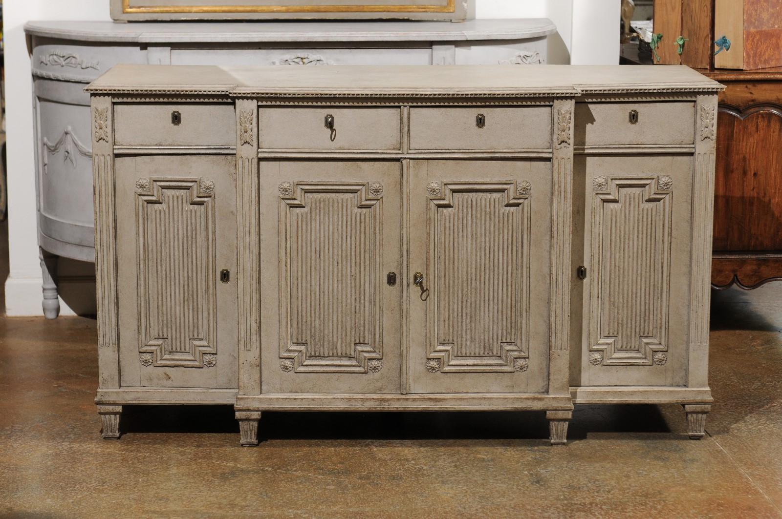 A Swedish Gustavian style painted wood breakfront sideboard from the 19th century, with dentil molding, fluted accents and carved rosettes. Born in Sweden during the 19th century, this stunning sideboard features a rectangular top with protruding