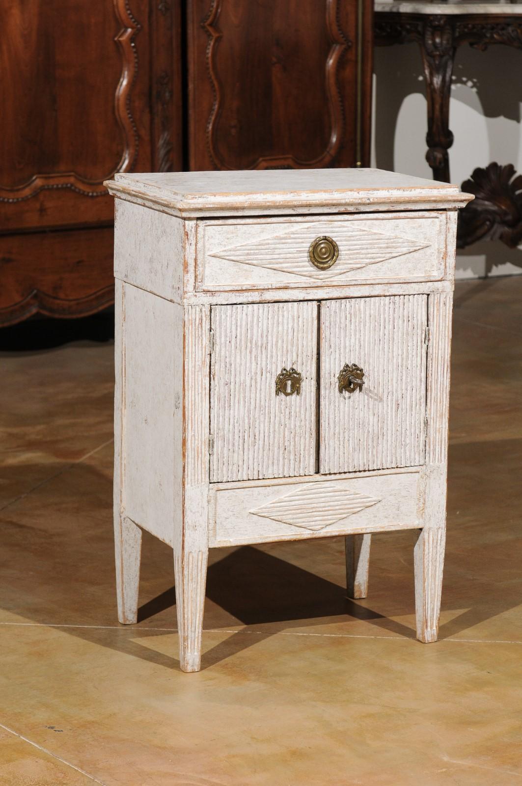 A Swedish Gustavian style painted wood nightstand cabinet from the 19th century, with diamond motifs and reeded patterns. Born in Sweden during the 19th century, this charming bedside cabinet features a slight raised rectangular top, sitting above a