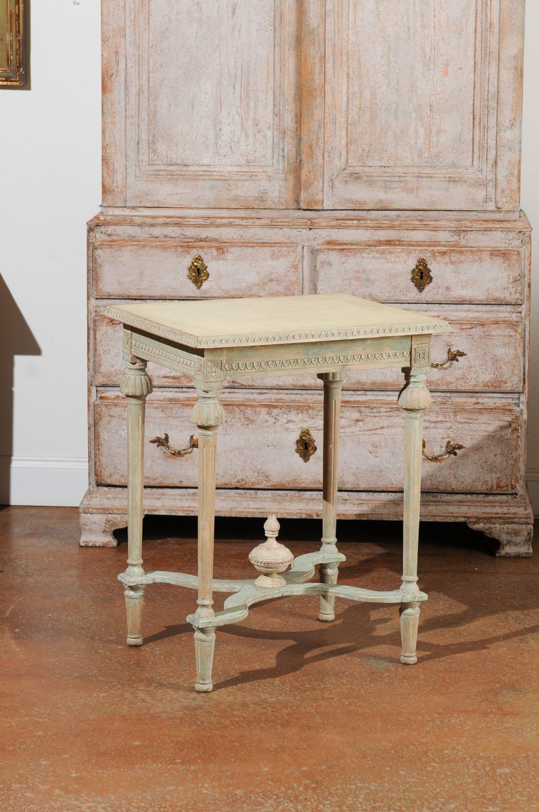 A Swedish Gustavian style painted wood console table from the 19th century, with carved waterleaves, X-form stretcher and finial. Created in Sweden during the 19th century, this painted console table features a rectangular top with a frieze of