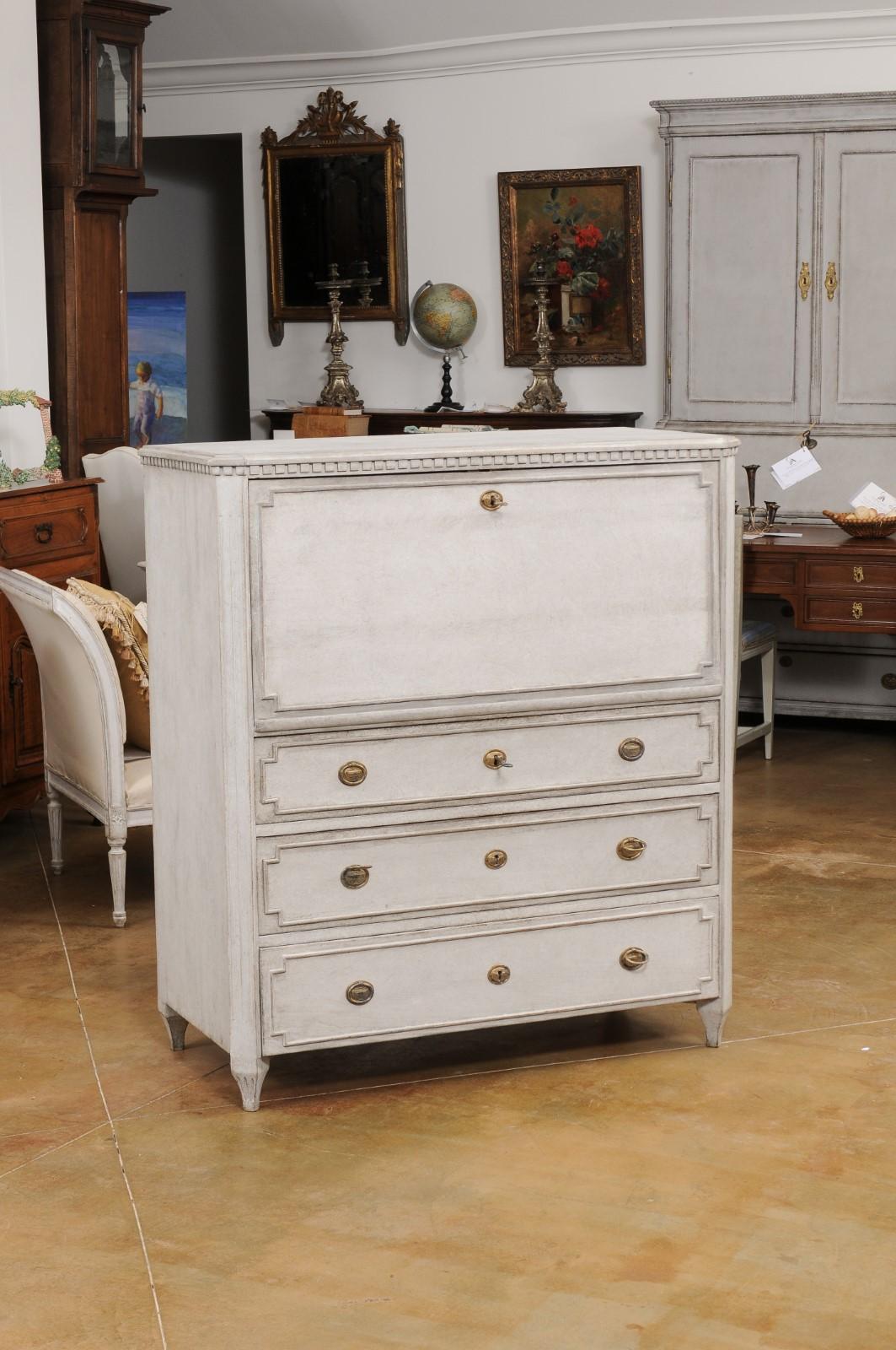 A Swedish Gustavian style painted wood drop-front secretary from the 19th century, with carved dentil molding, multiple inner drawers and three long graduated drawers. Created in Sweden during the 19th century, this painted secretary showcases the