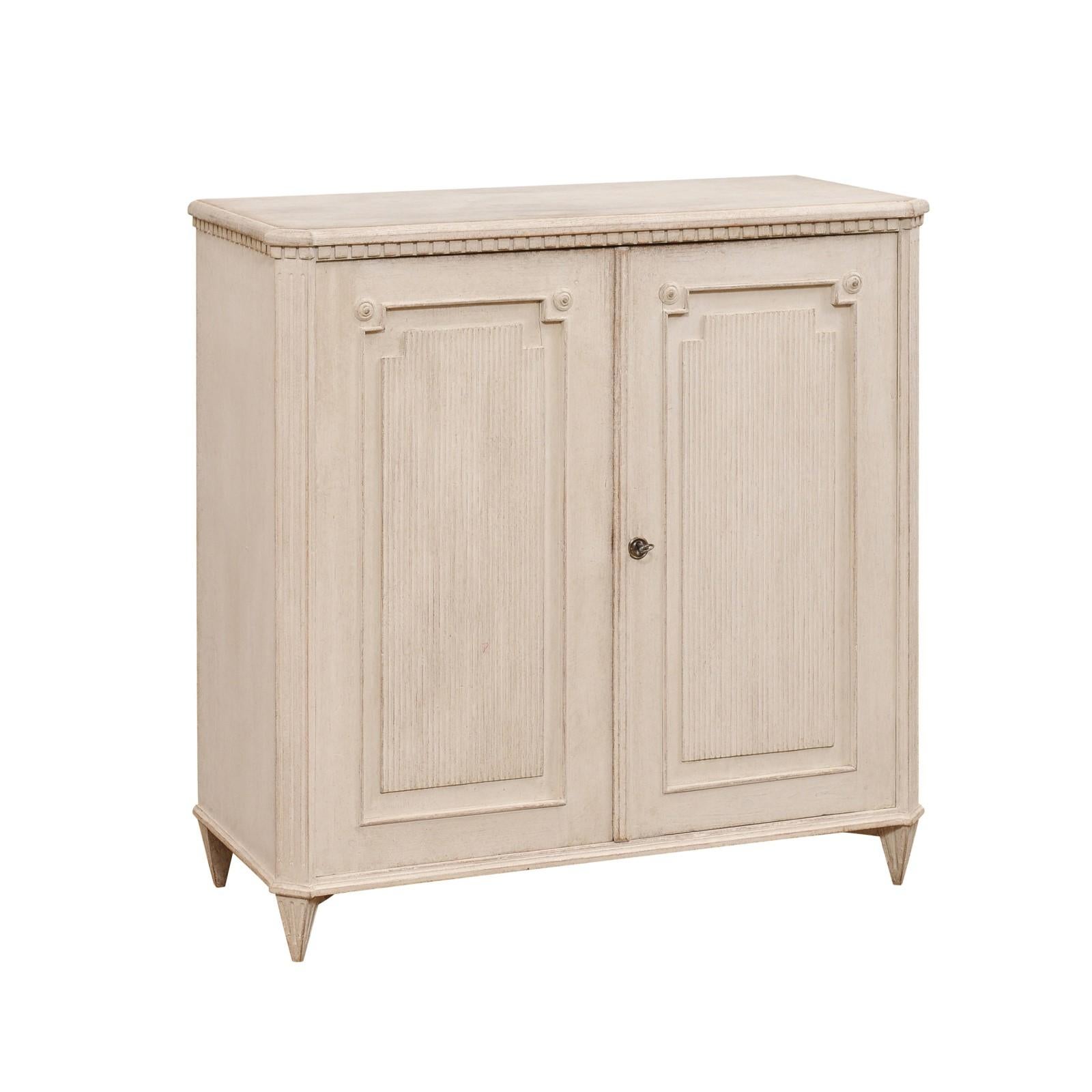 A Swedish Gustavian style painted wood sideboard from the 19th century with carved dentil molding, two doors with reeded accents and short tapered feet. Beautify your space with this 19th-century Swedish Gustavian style painted wood sideboard, a