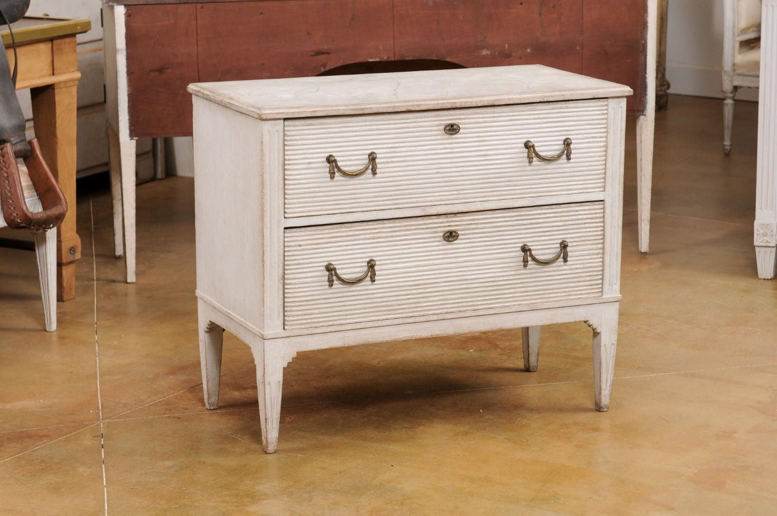 A Swedish Gustavian style painted wood chest from the 19th century with two drawers, carved reeded accents, swag hardware, marbleized top and tapered legs. Created in Sweden during the 19th century, this painted wood chest showcases the stylistic