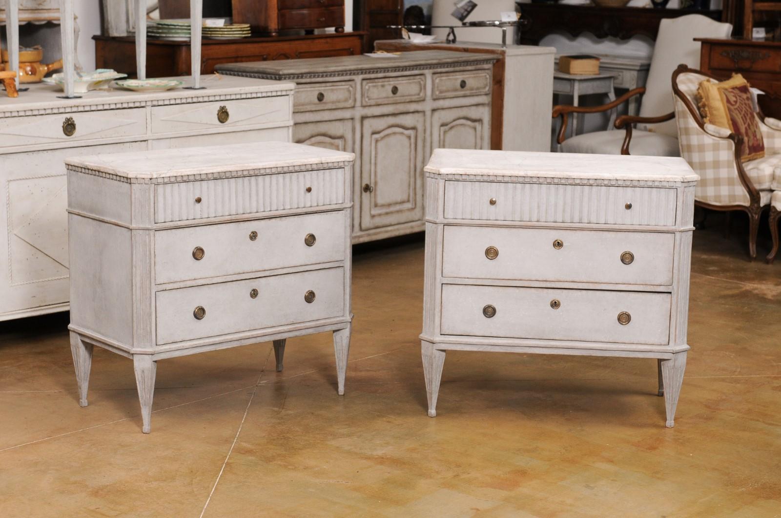 A pair of Swedish Gustavian style painted wood commodes from the 19th century, with marbleized tops and dentil moldings. Created in Sweden during the 19th century, each of this pair of Gustavian style commodes features a faux marble top with canted