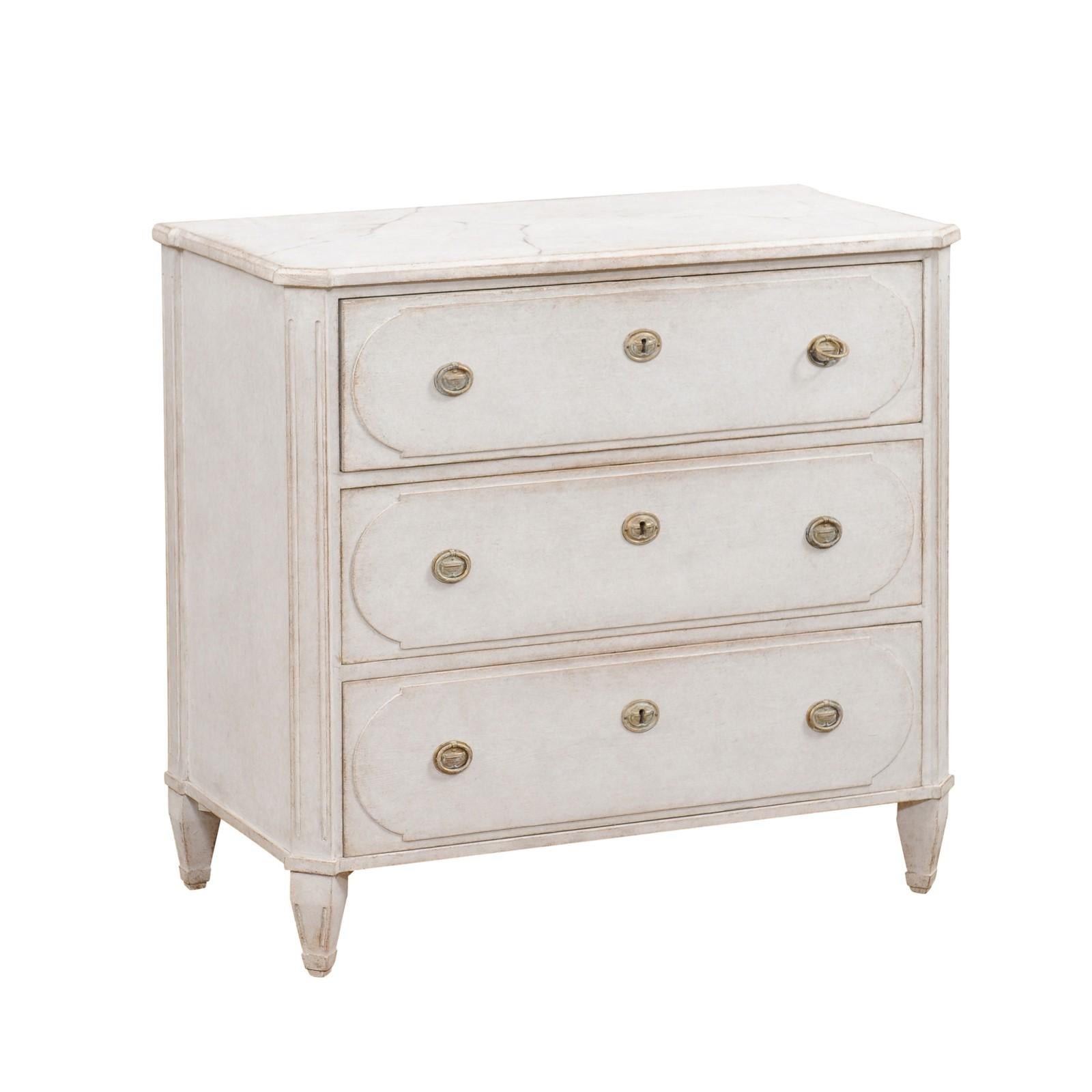 A Swedish Gustavian style three-drawer chest from the 19th century with light gray painted finish, marbleized top and fluted side posts. This 19th-century Swedish Gustavian style chest is a testament to timeless elegance, graced with a light gray
