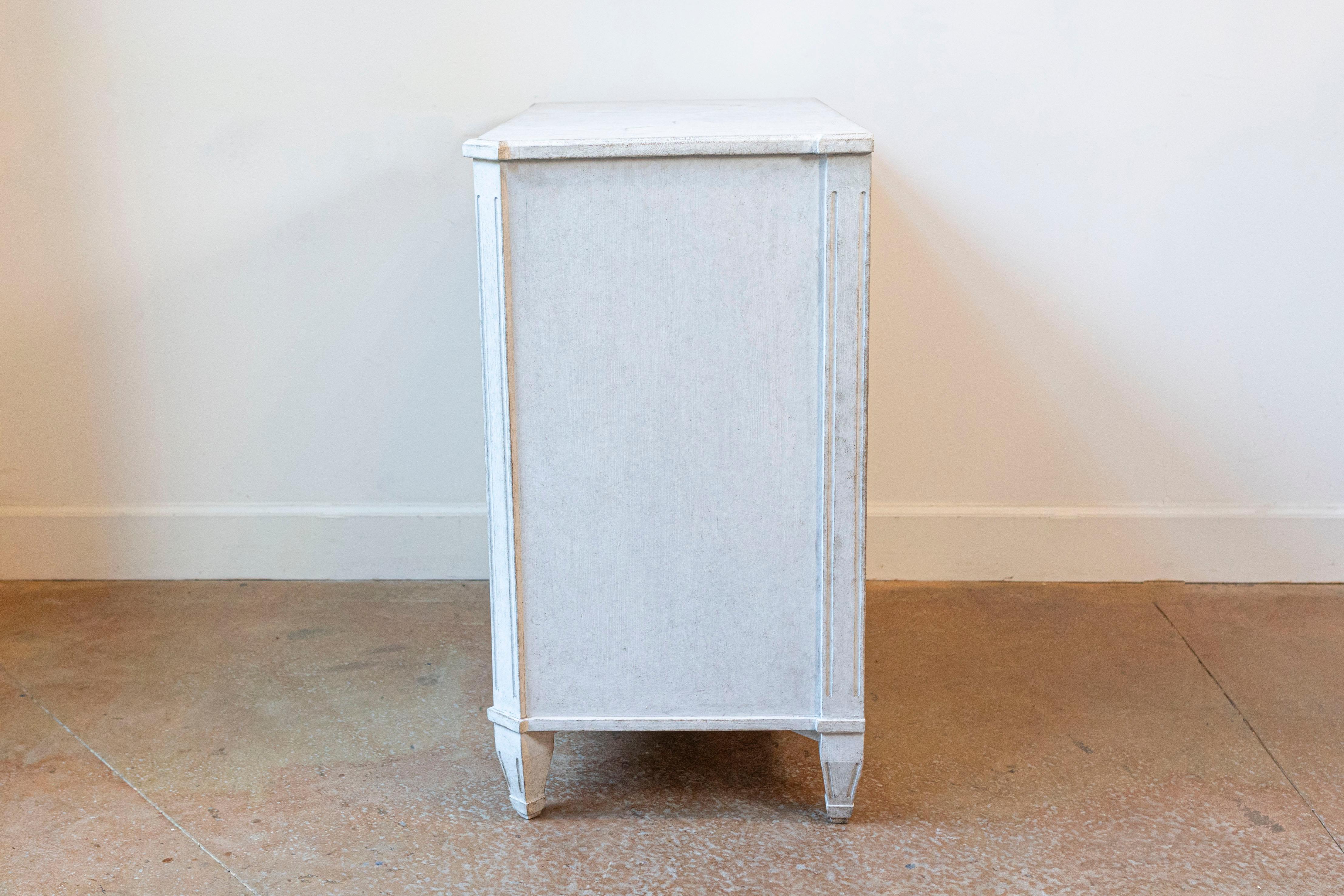 Cassettone a tre cassetti in stile gustaviano svedese del XIX secolo con finitura verniciata grigio chiaro, piano marmorizzato e montanti laterali scanalati. Questa cassapanca in stile gustaviano svedese del XIX secolo è una testimonianza di