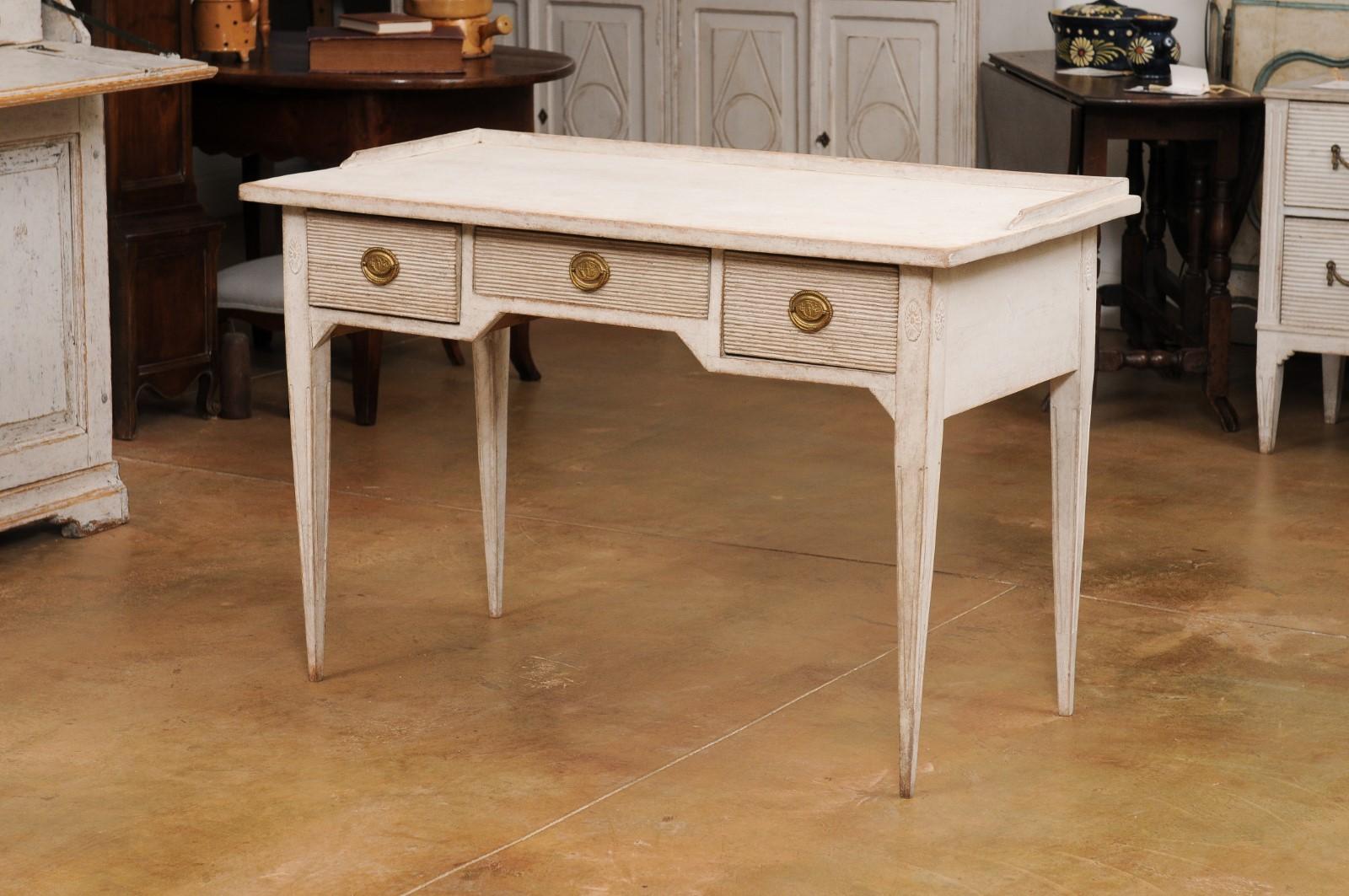 A Swedish Gustavian Style painted wood writing desk from the 19th century with three reeded drawers, brass hardware, carved rosettes and tapered legs. Experience the charm of Scandinavian elegance with this 19th century Swedish Gustavian Style