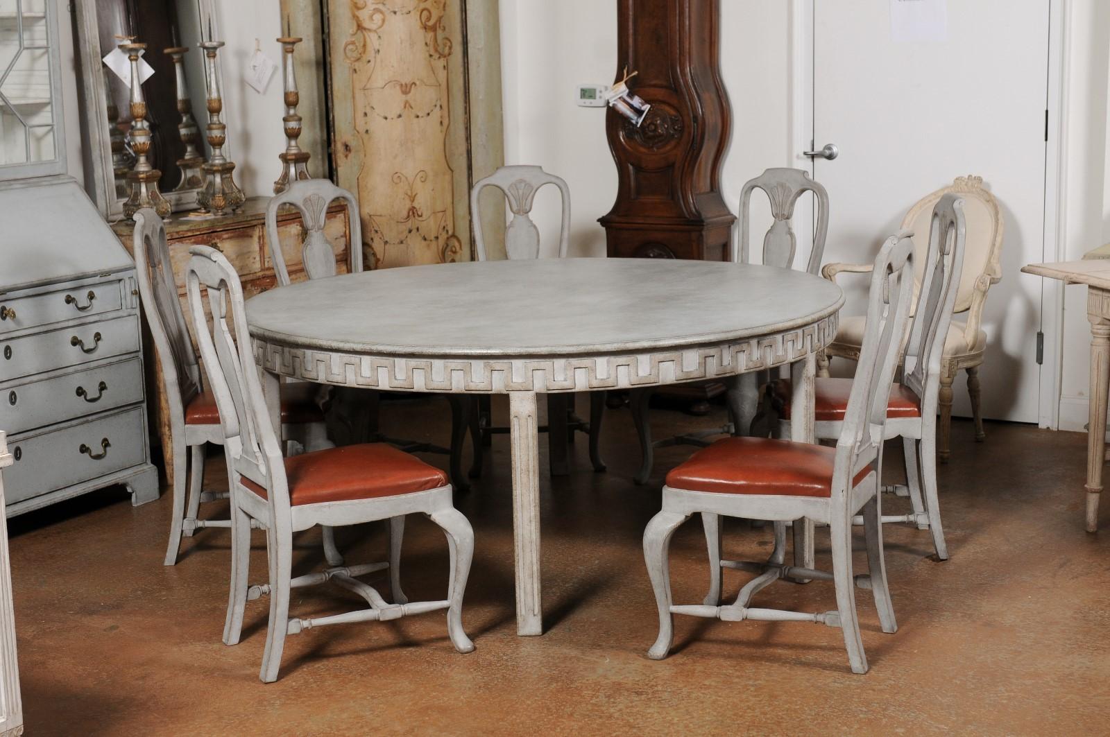 A Swedish Gustavian style painted wood dining table from the 20th century, with carved meander frieze and fluted legs. Created in Sweden during the 20th century, this painted table features a circular top sitting above an exquisite carved meander