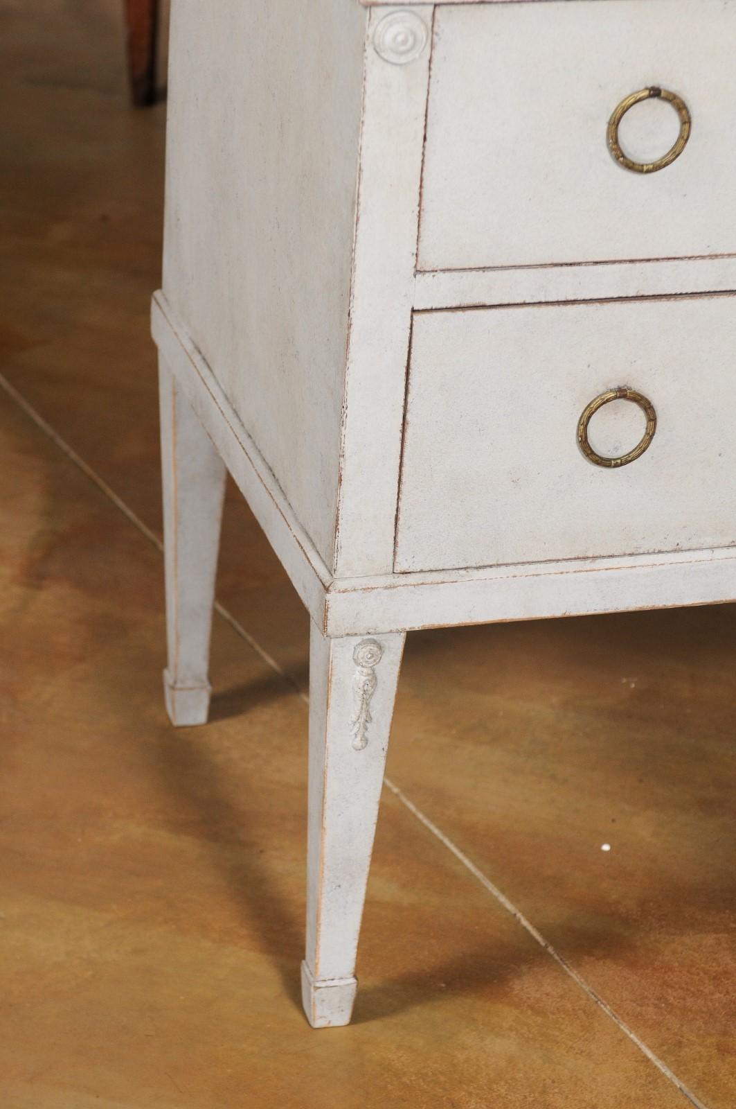 A Swedish Gustavian style chest of drawers from the 20th century with tapered legs and carved medallions. Charming our eyes with its clean lines and soft finish, this Gustavian style chest features a rectangular top sitting above two drawers each