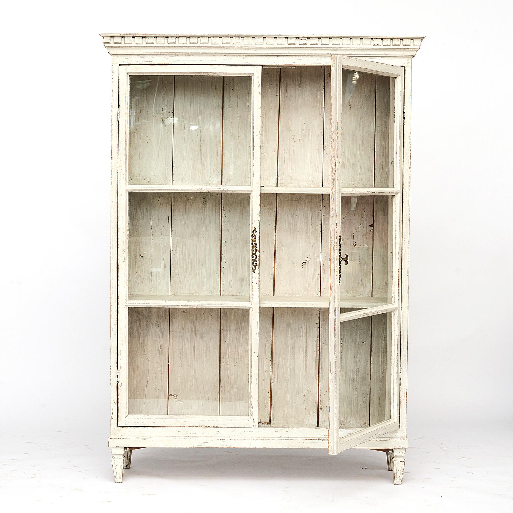 Swedish Gustavian style cabinet with a pair of paned glass doors. Cornice accented with dentil moldings, resting on four fluted tapering legs.
Closure of the doors in the form of the handle.
Later professionally antique repainted in grey-white