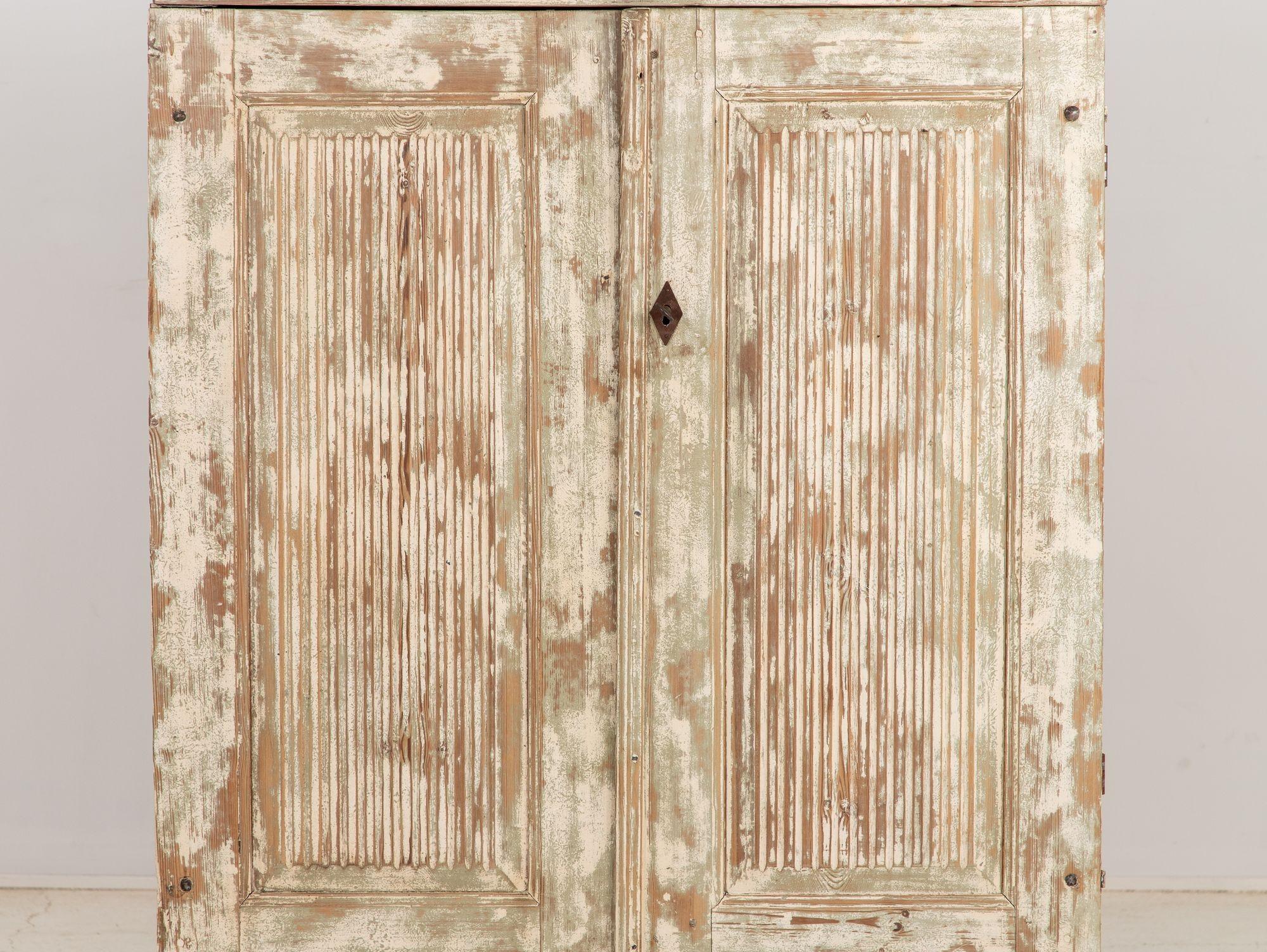 Immerse yourself in the timeless elegance of late 19th Century Swedish Gustavian style with this exquisite cabinet. Crafted from painted pine wood, it exudes understated sophistication. The two reeded doors add a subtle textural dimension, while