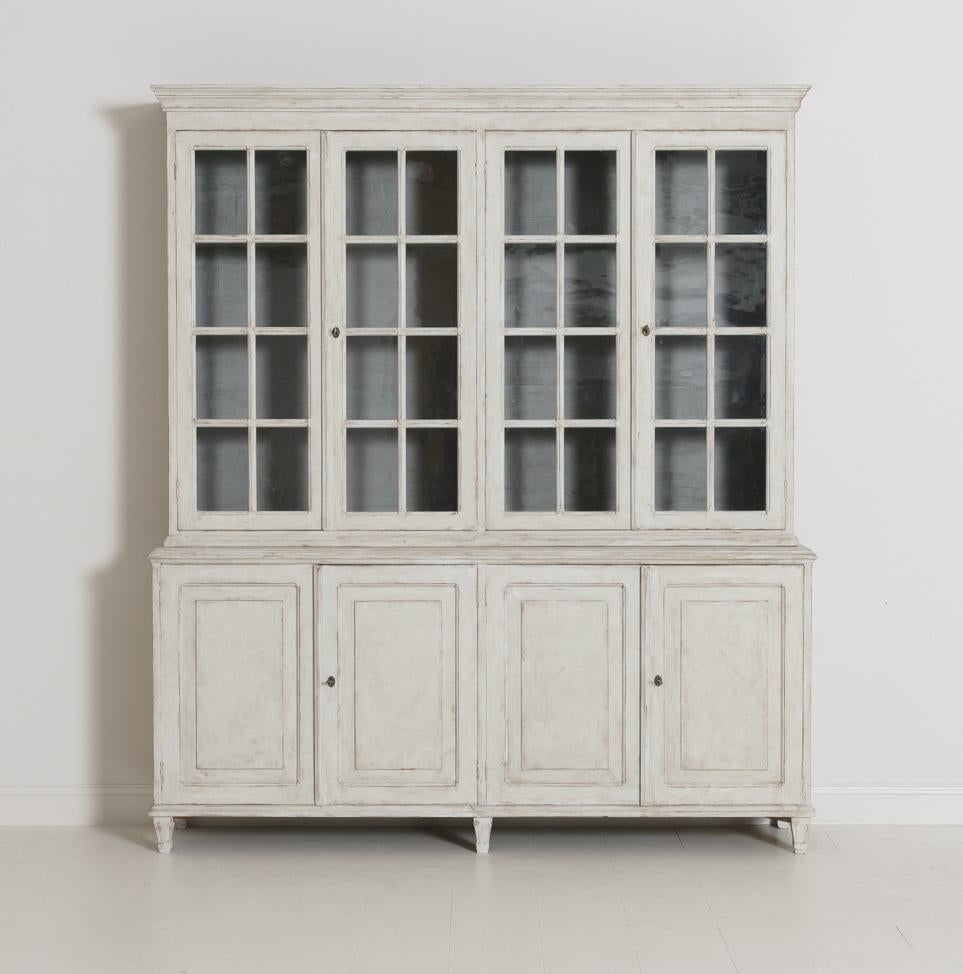 A beautiful Swedish Gustavian Style four-door painted vitrine cabinet. This bookcase is made in two parts. The upper section has three fixed shelves behind original glass doors. The shelf depth is 10 inches. The distance between shelves starting
