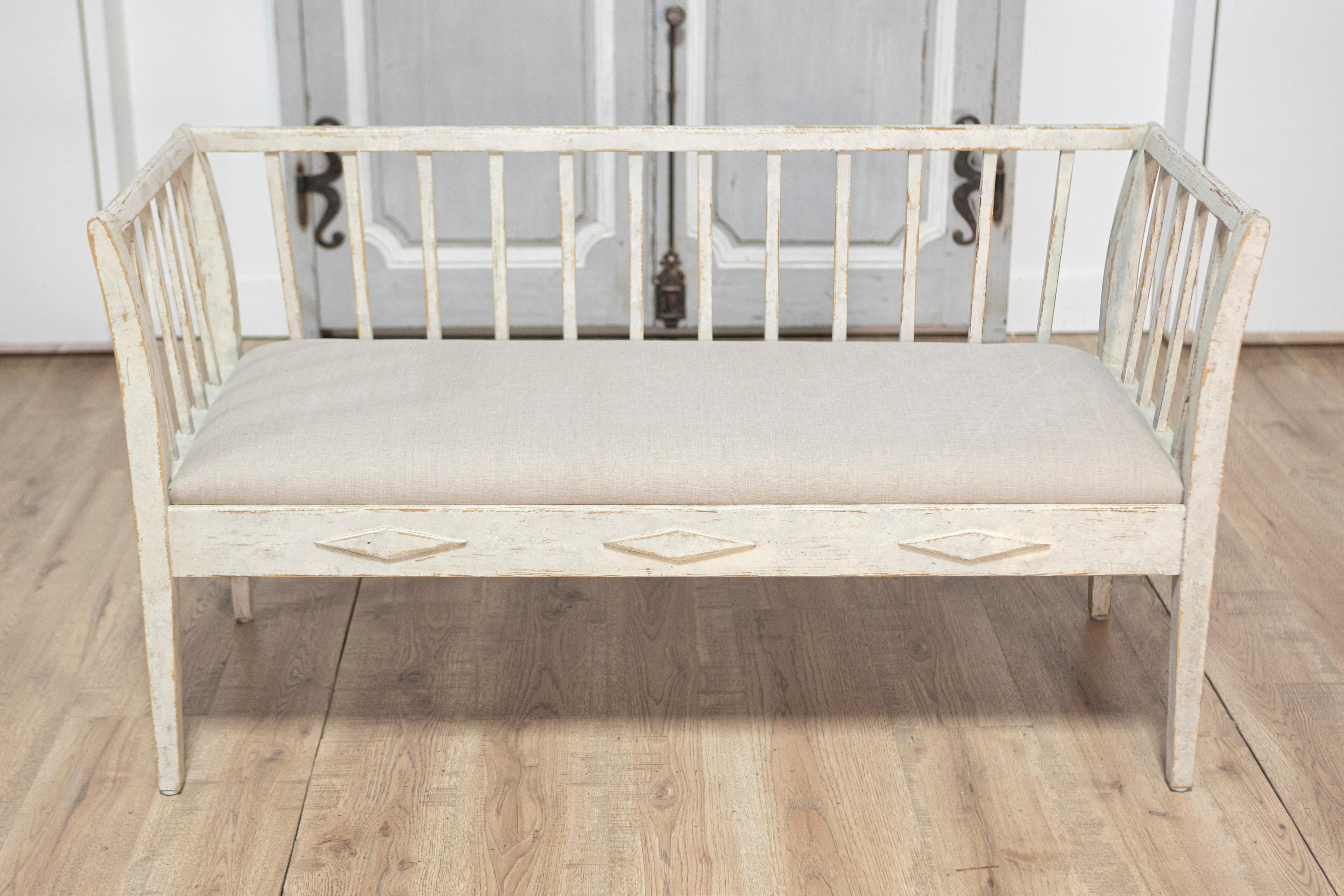 A Swedish Gustavian style gray painted sofa bench from the 20th century with high back, raised diamond motifs and linen upholstery. This Swedish Gustavian style sofa bench captivates with its elegant simplicity and timeless charm. Painted in a light