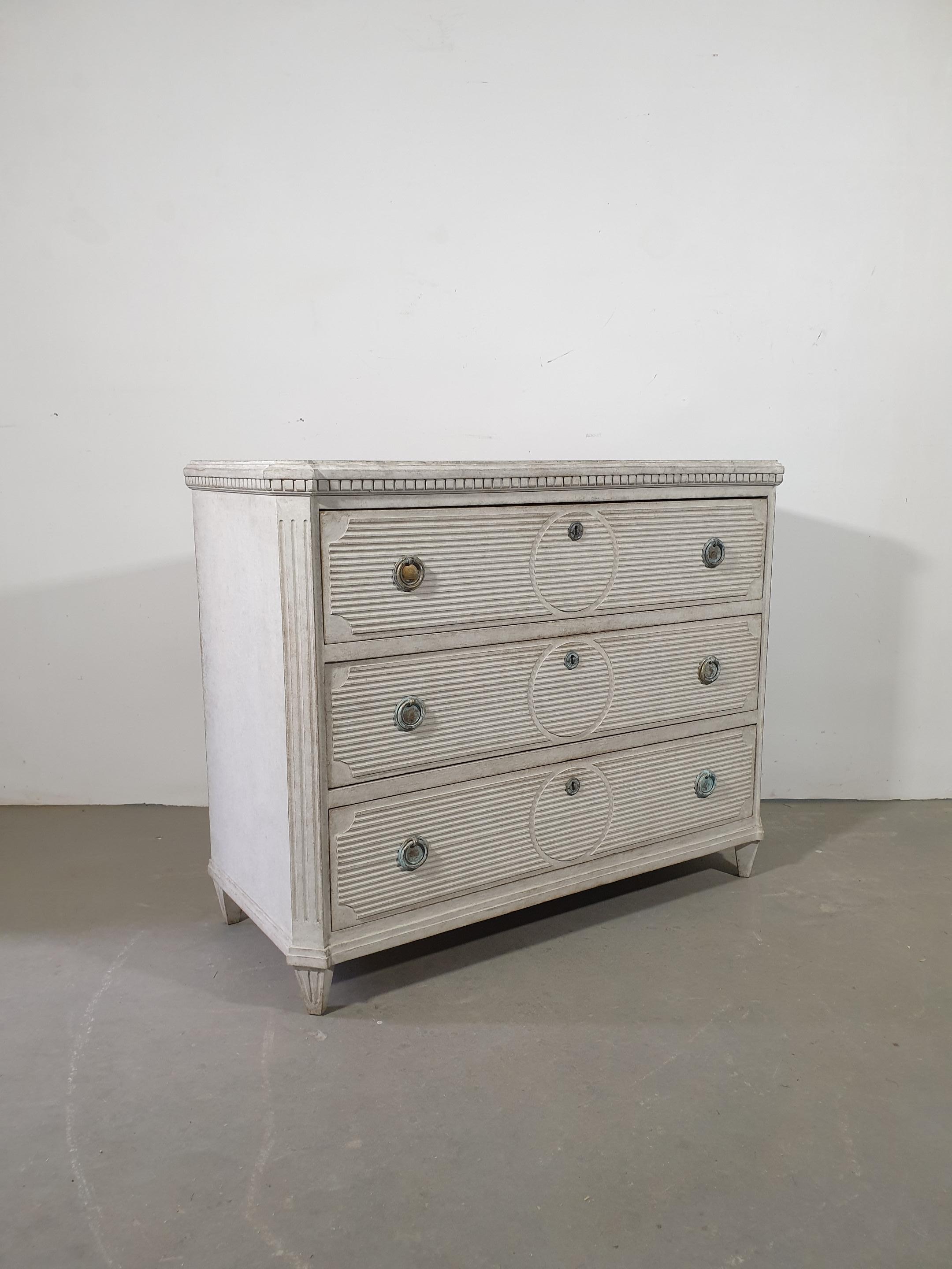 A Swedish Gustavian style three-drawer chest from the 19th century, with marbleized top, gray painted finish, reeded panels and fluted side posts. This 19th-century Swedish Gustavian style three-drawer chest beautifully captures the essence of