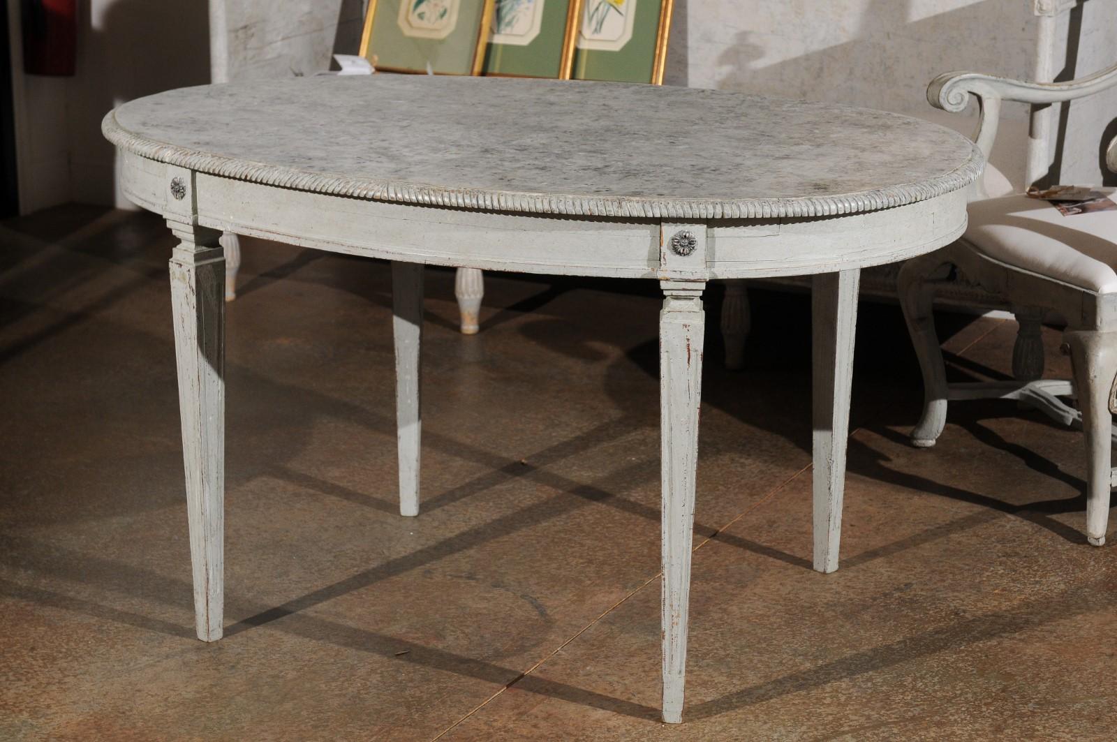 A Swedish grey painted Gustavian style wooden table from the late 19th century, with oval marbleized top, tapered legs, rosettes and distressed finish. Born in Sweden during the later years of the 19th century, this exquisite oval table features the
