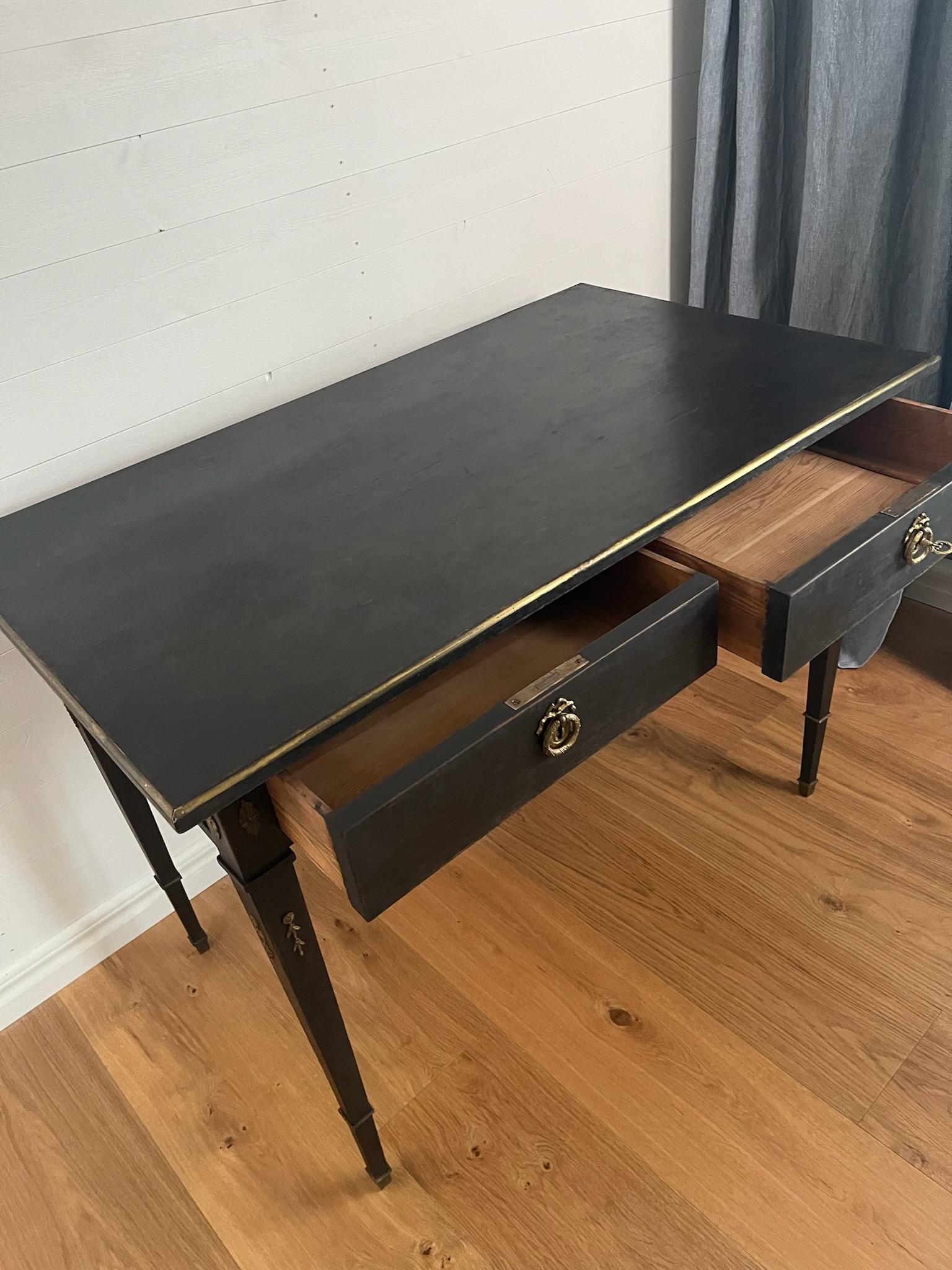 A Swedish Gustavian style desk from circa 1890 painted finish, two drawers, Classic legs tapering downwards  with stunning brass details.

The desk is handpainted in black / brown color in traditional scandinavian way with reel patina feeling.

The