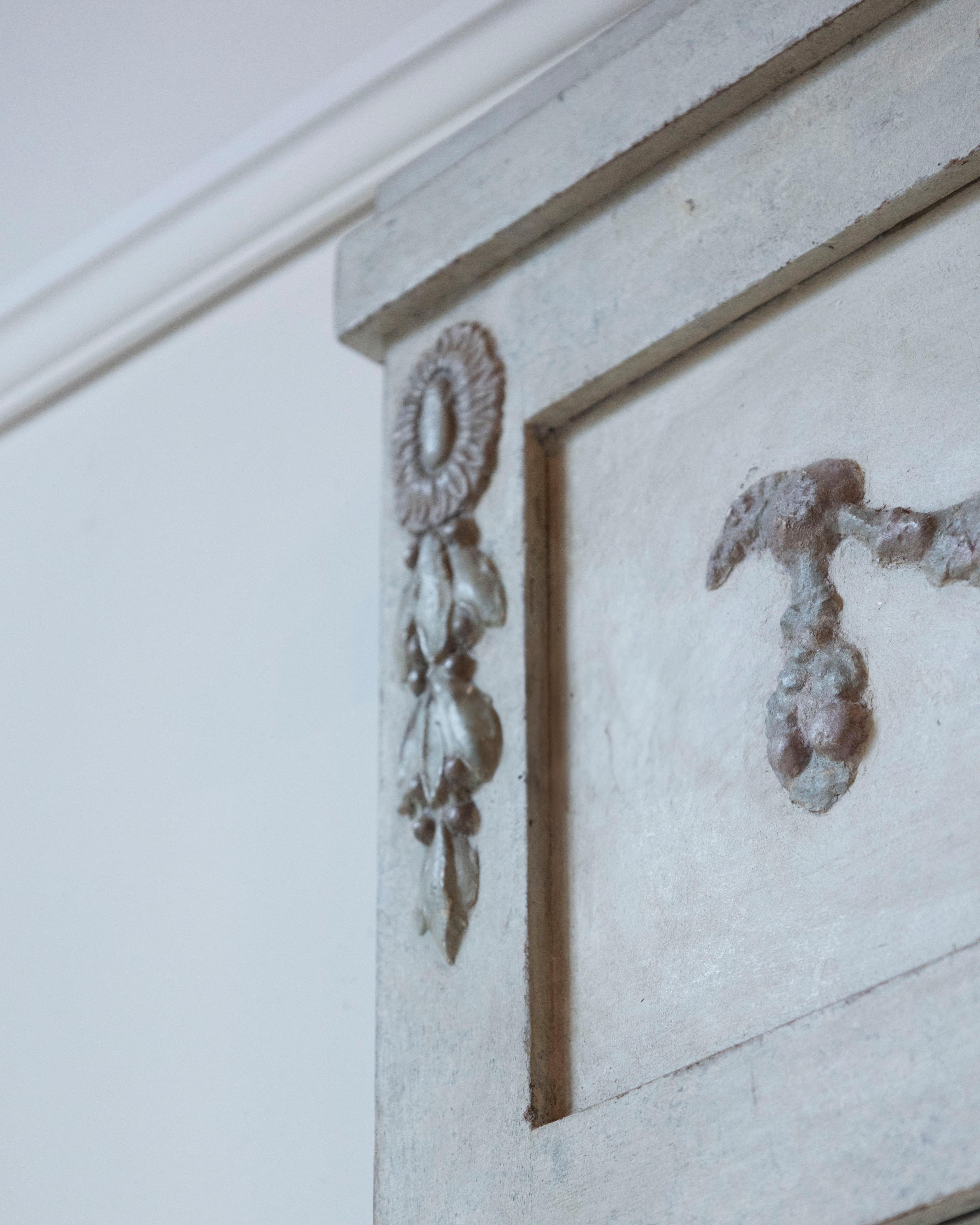 A finely detailed Swedish mirror in the Gustavian style, circa 1920. The rectangular frame is crowned with an elegant frieze featuring a carved garland and leaf motif, painted in delicate tones of pale pink and withered green. The base color is a