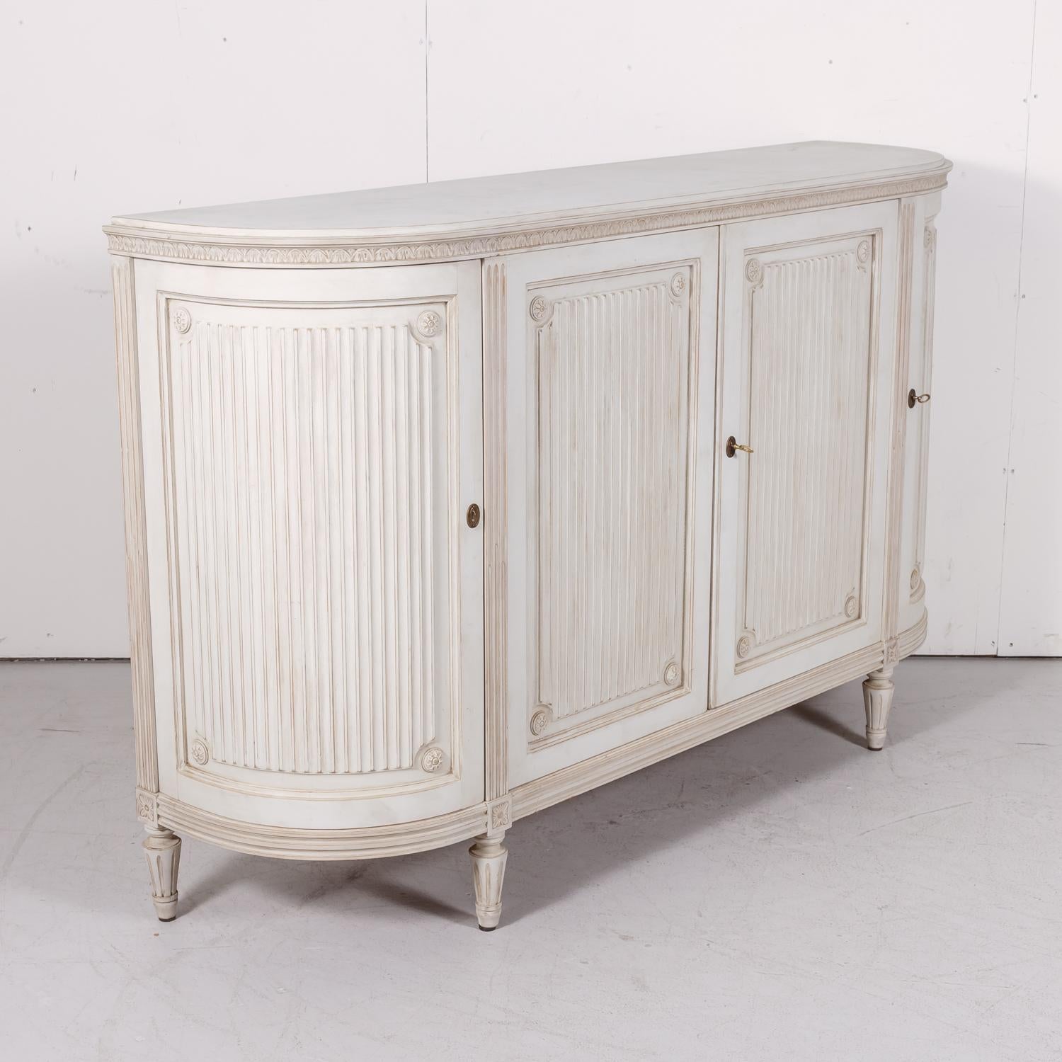 A mid-20th century Swedish Gustavian style painted enfilade buffet with lovely curved sides, circa 1950s. Having four hand reeded panel doors with carved rosettes in the corners, the center doors of this lovely vintage enfilade open to reveal a