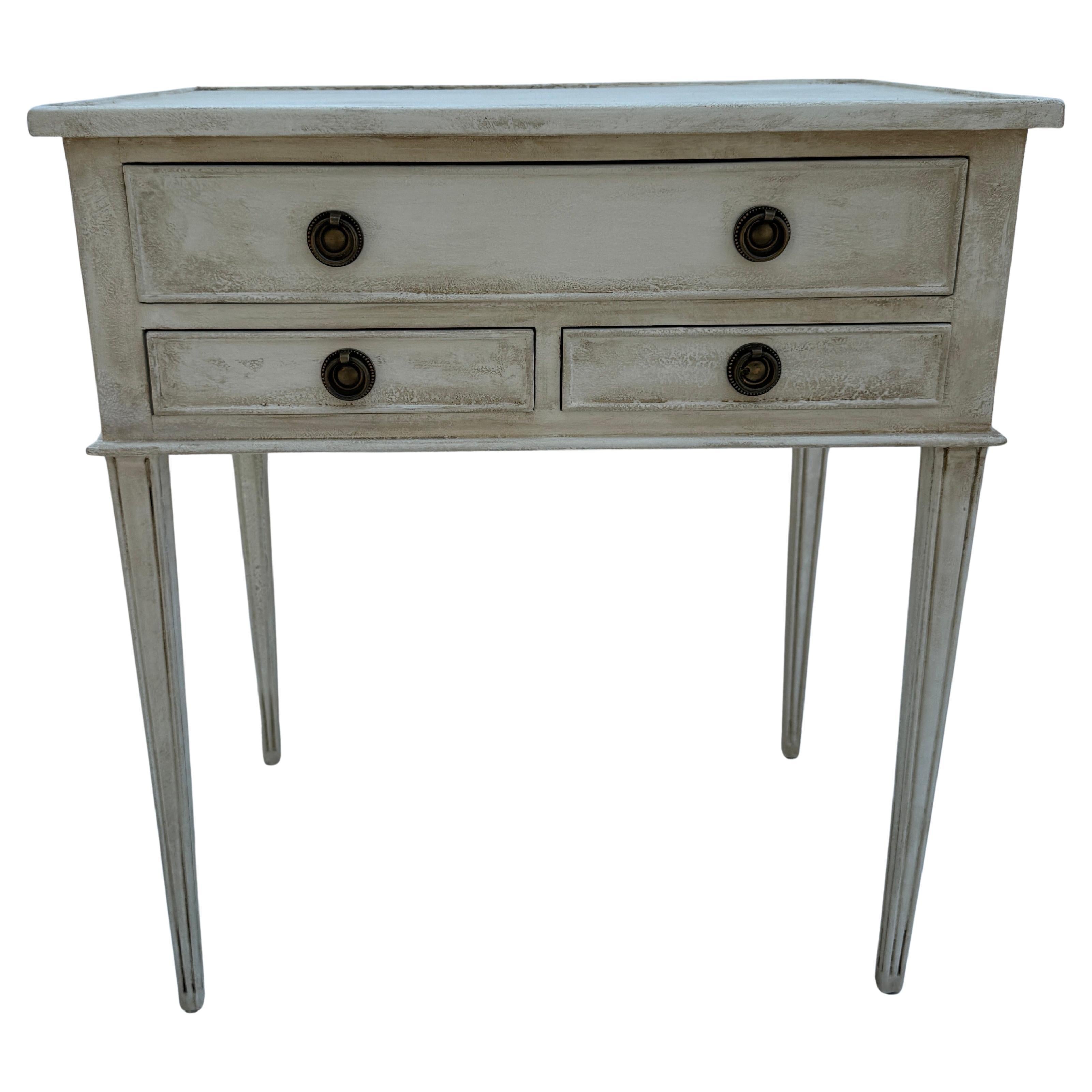 This Swedish style three drawer hand painted neutral toned bedside tables has been constructed from solid wood. Classic details on the table including a hand-applied finish and feature bronzed ring hardware. This piece has been based on an 18th