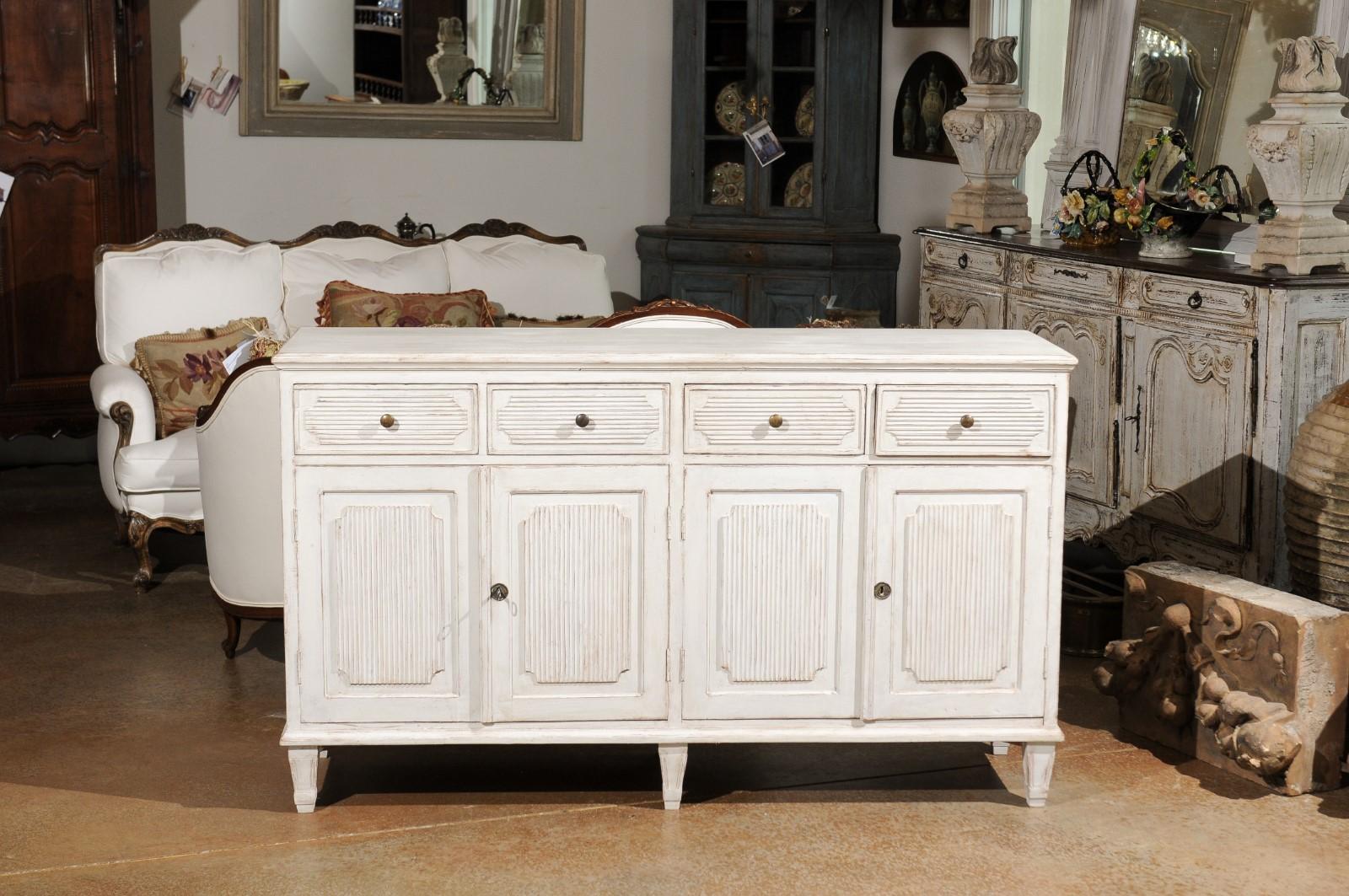 A Swedish painted wood sideboard from the 20th century, with reeded accents and four drawers over four doors. Born in Sweden during the 20th century, this exquisite painted sideboard features a rectangular top sitting above four drawers with reeded
