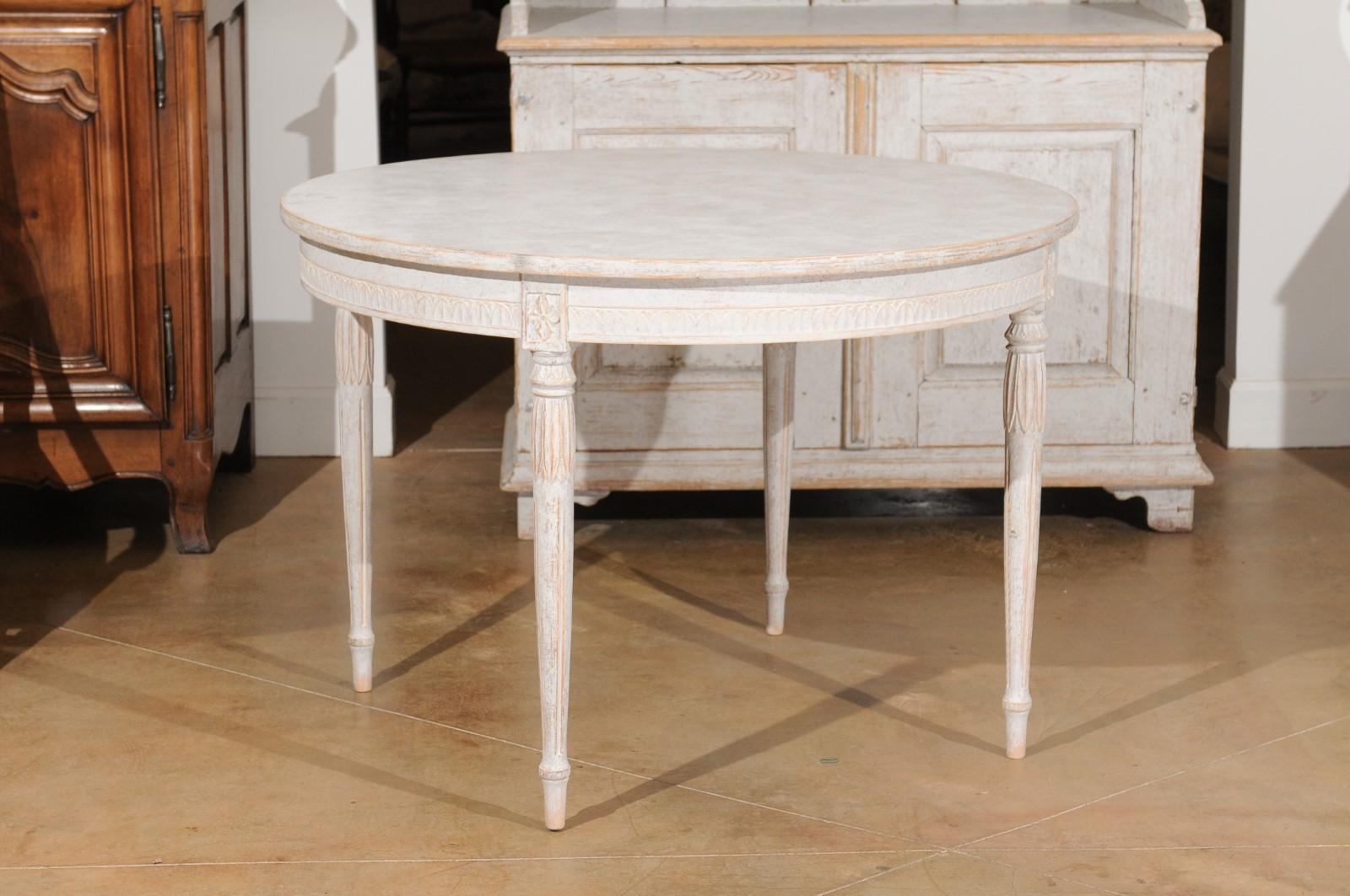 A Swedish Gustavian Style painted table from the 20th century, with circular top and fluted legs. Created in Sweden during the 20th century, this Gustavian Style table features a round top sitting above an elegant apron adorned with a frieze of