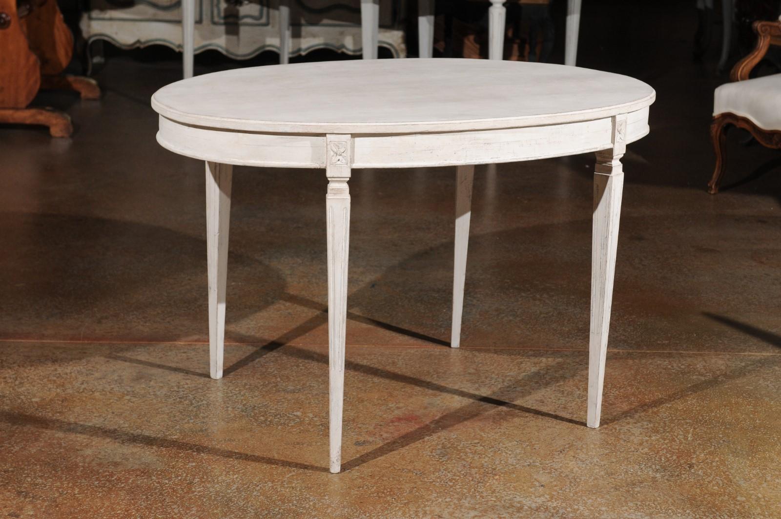 A Swedish Gustavian style painted oval table from the late 19th century with carved rosettes and tapered legs. Born in Sweden during the later years of the 19th century, this table presents the stylistic characteristics of the Gustavian period.