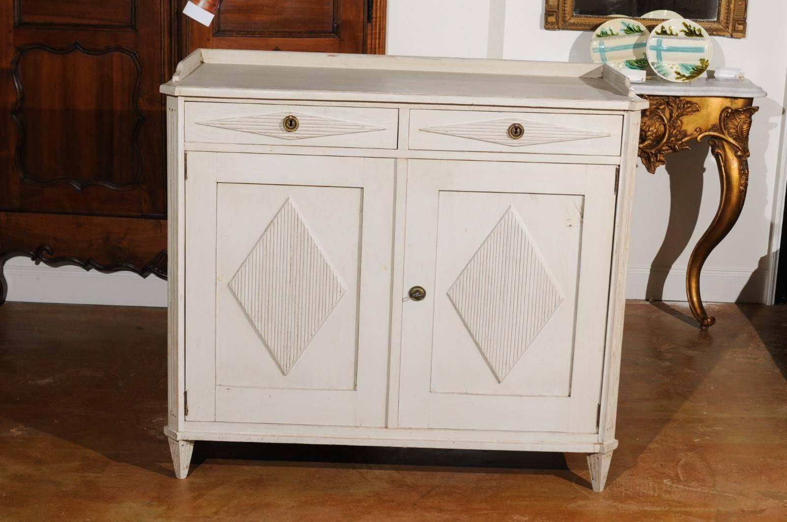 A Swedish Gustavian style painted wood sideboard from the late 19th century, with reeded diamond patterns and two drawers over two doors. This Swedish painted sideboard features a rectangular top with canted corners in the front, surrounded by a