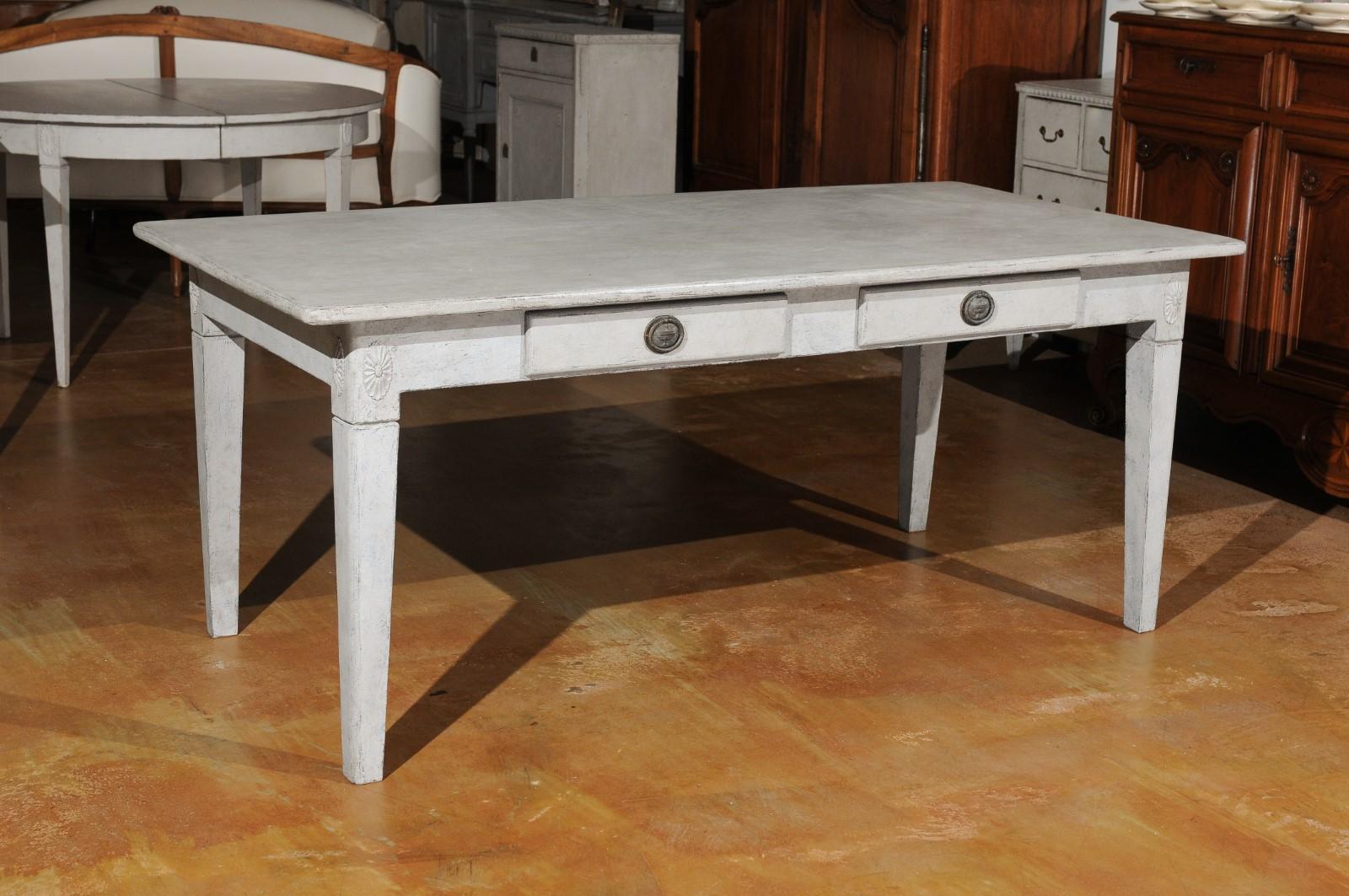 A Swedish Gustavian style painted wood table from the 20th century, with two drawers and carved rosettes. Created in Sweden during the early 20th century, this painted table features a rectangular top sitting above two drawers fitted with classical