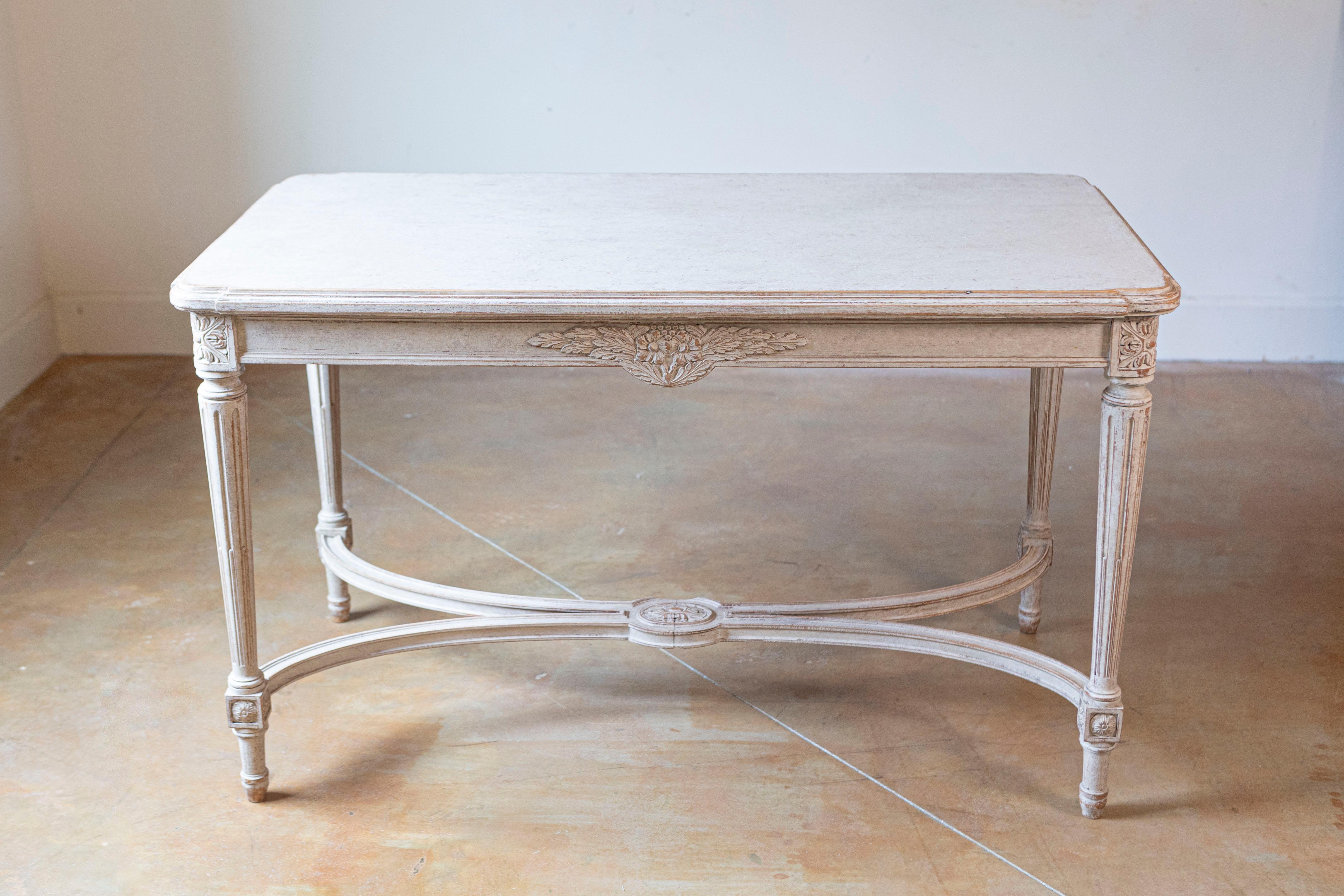A Swedish Gustavian style painted wood coffee table with fluted legs and cross stretcher from the early 20th century. This Swedish coffee table features a rectangular top with beveled edges and rounded corners, sitting above an exquisitely carved