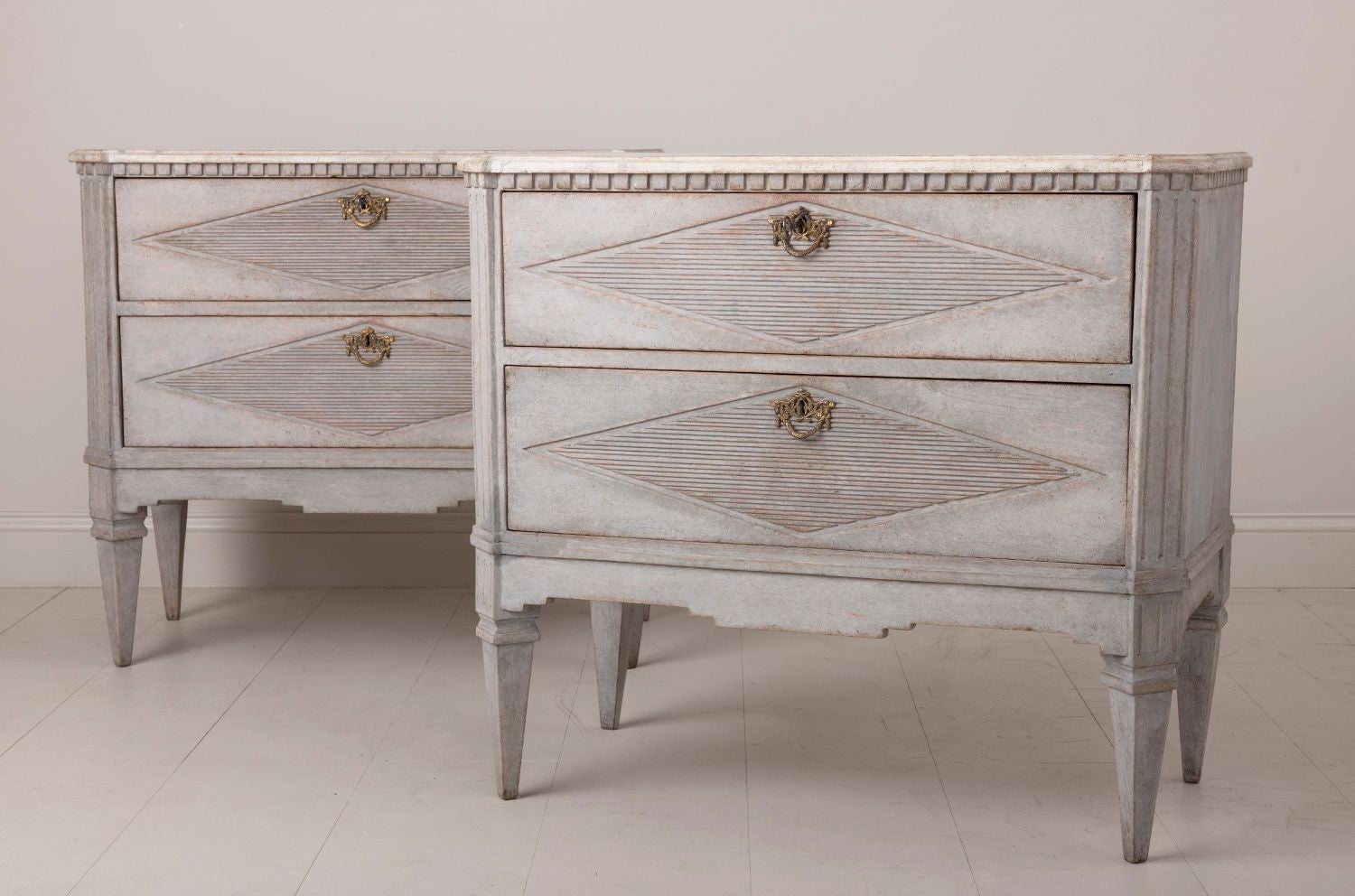 A pair of Swedish commodes in the Gustavian style with hand-painted marbleized tops. These chests have beautifully reeded drawer fronts with a lozenge design. Two large drawers, brass hardware, dentil molding around the top, canted and fluted corner