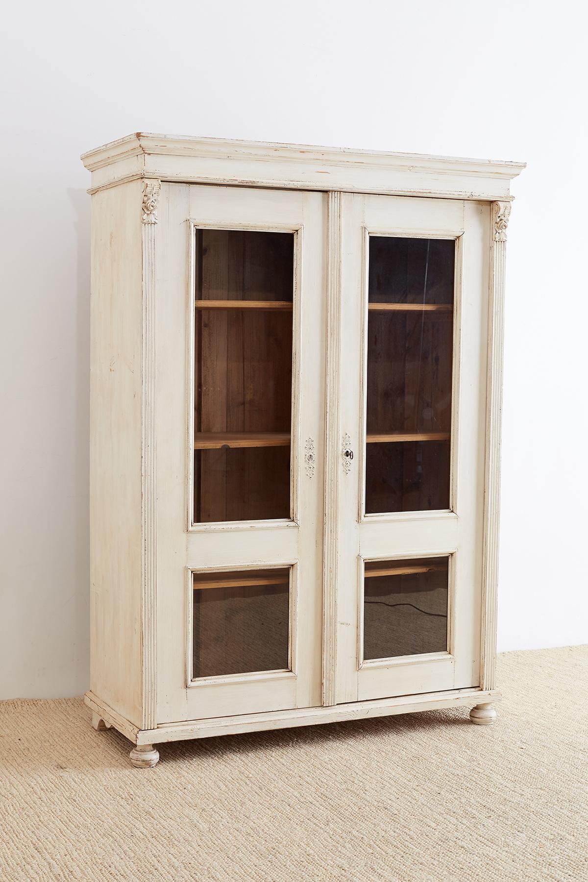 Gorgeous painted pine bibliotheque bookcase or linen press made in the neoclassical Swedish Gustavian style. Features a two glazed door case with fluted pilasters on each side supporting the corniced top. The interior is fitted with four shelves and