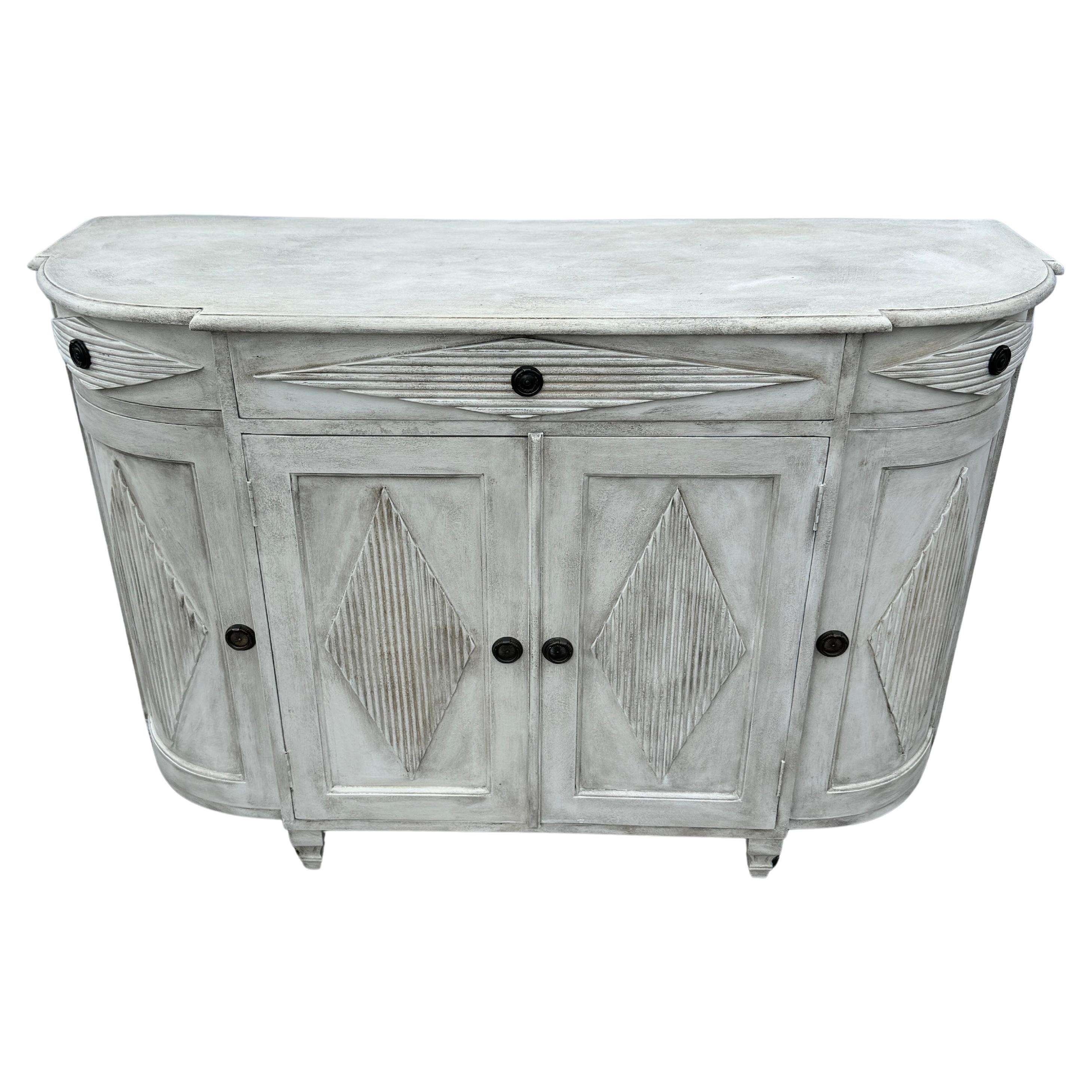 White Painted Gustavian 3 Drawer Painted Commode Cabinet with Doors

Hand painted Gustavian style sideboard constructed from solid wood with a hand-applied distressed finish with brass ring hardware. This classic Swedish style commode with