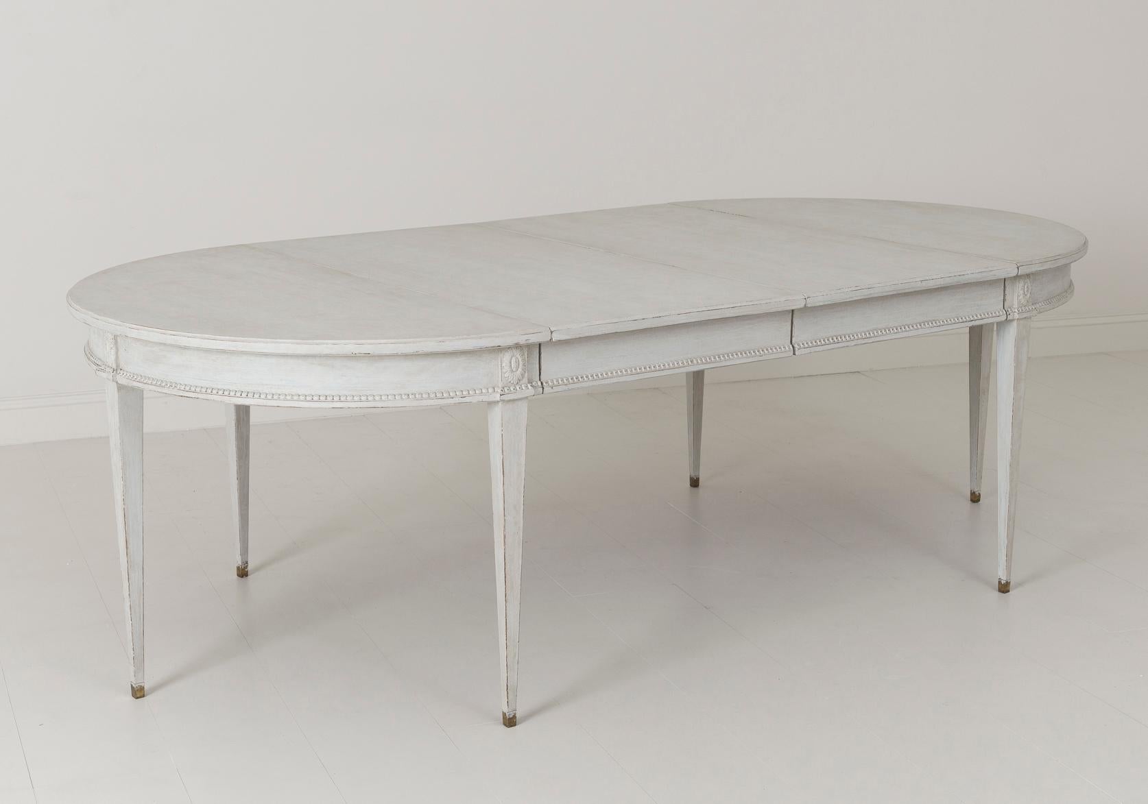 A beautiful Swedish two-leaf oval dining table in the Gustavian style. The patina is a blend of light gray and aged white. This is a charming and versatile table that can extend with one or two leaves. The table rests upon square, tapered, and