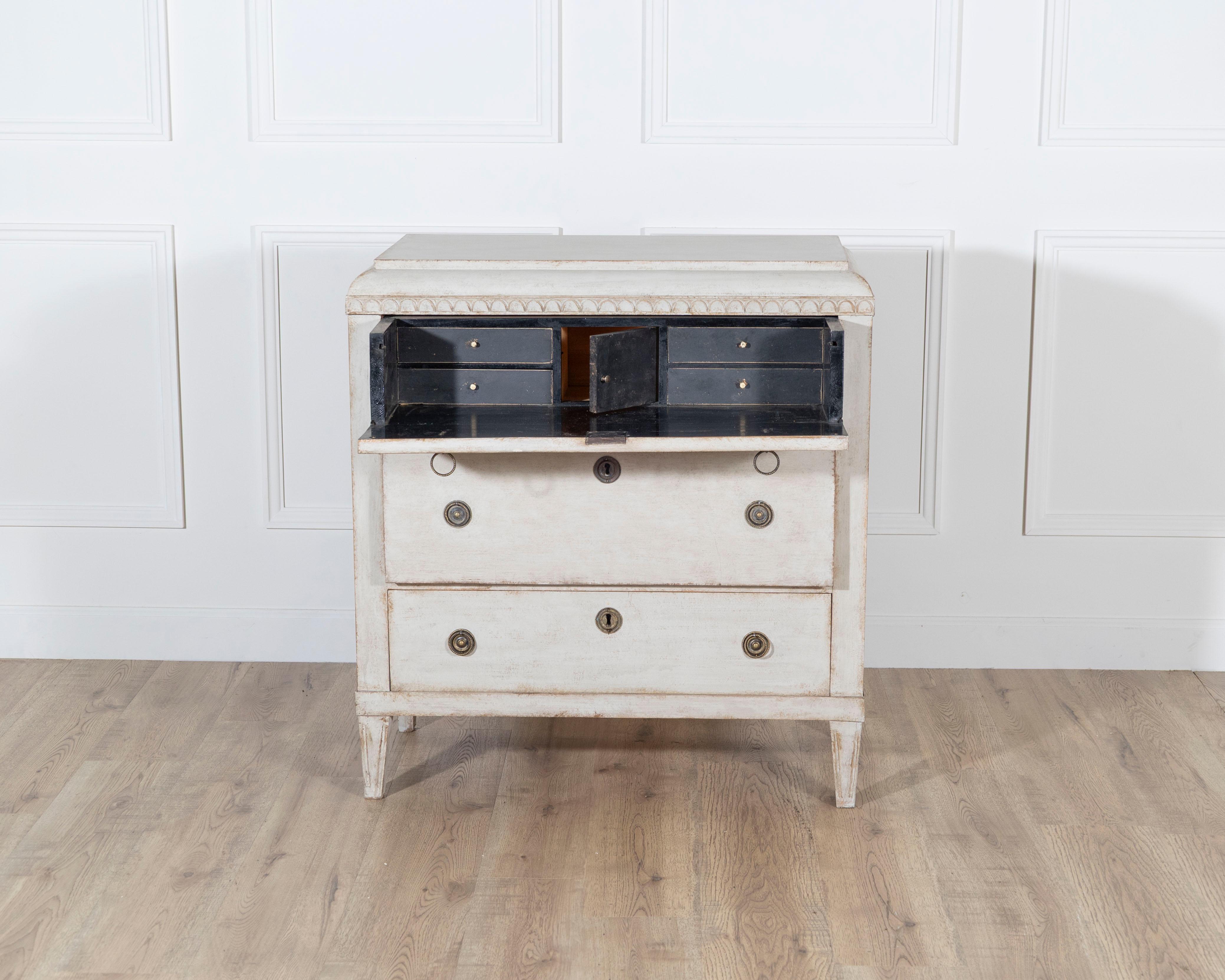 A charming Swedish Gustavian writing chest of drawers, circa 1840–1850, featuring a hidden writing compartment ingeniously concealed behind the upper drawer front. Crafted in solid pine and finished in a soft, chalky white patina, this piece