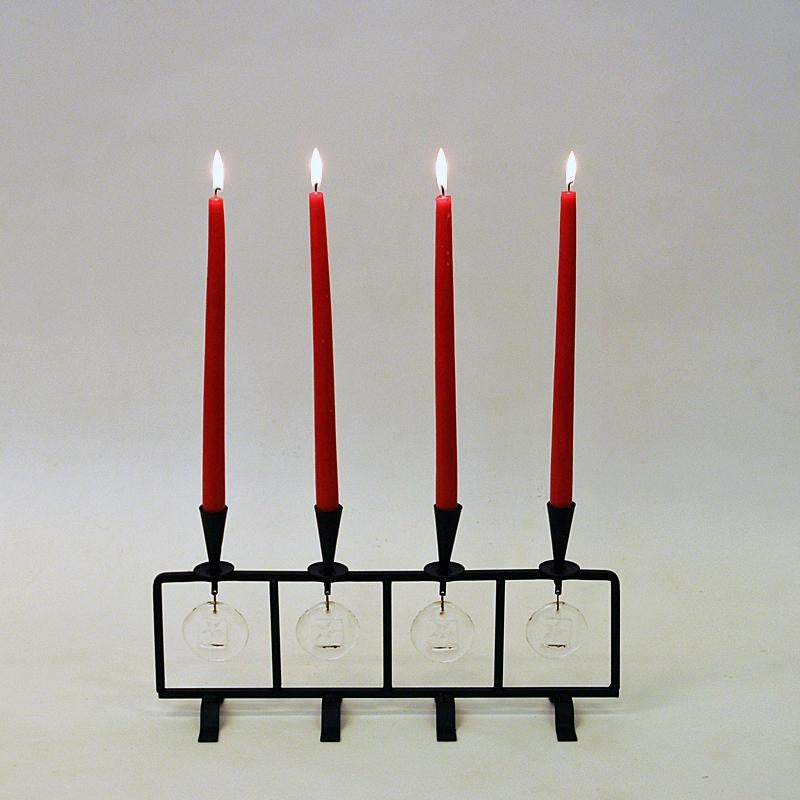 Lovely black forged iron candle holder by Erik Höglund for Boda 1960s - Sweden. 
The candleholder has four candle holder cups and four round glass plate decorations hanging underneath every cup with a little star in the middle. The candle holder is