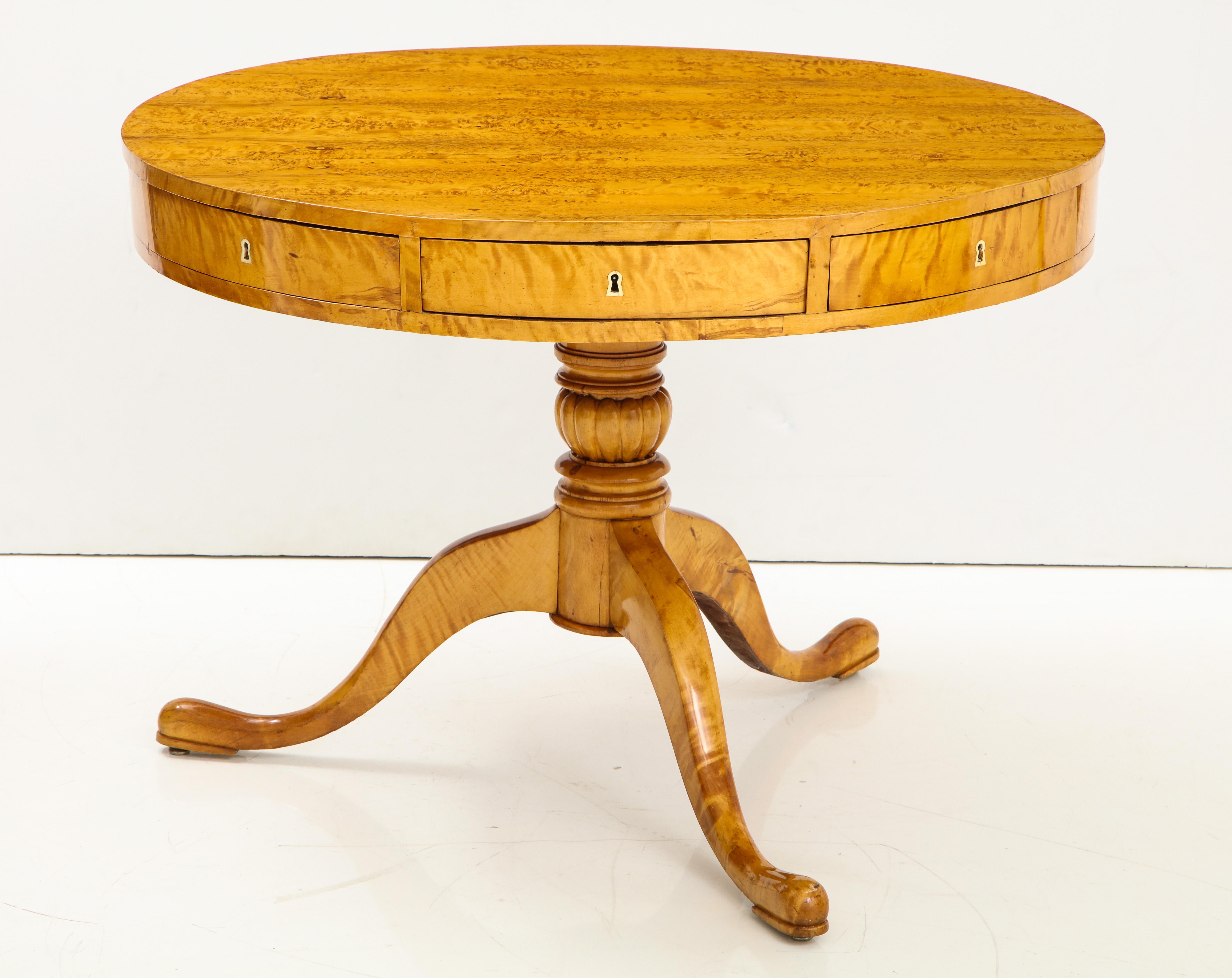 A Swedish Karl Johan birch and birch root center table, circa 1830s, the well figured circular top above a plain frieze with four true drawers and four pie shaped drawers, raised on a circular turned pedestal with gadrooned banding, ending with
