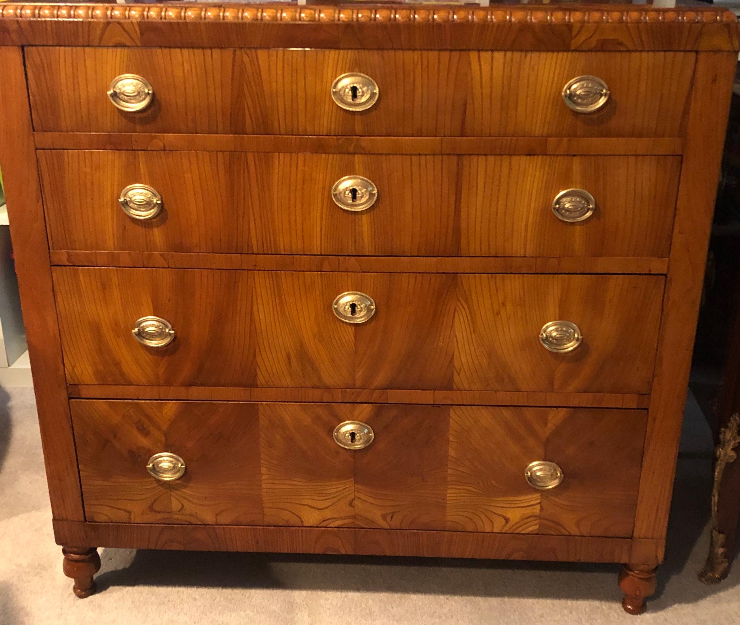 Elegant Karl Johan chest of drawers, Sweden 1830, mirrored elm wood veneer with original brass fittings. The four-drawer commode is decorated with a pearl frieze on the border of its top. It is in very good refinished condition, French polished.