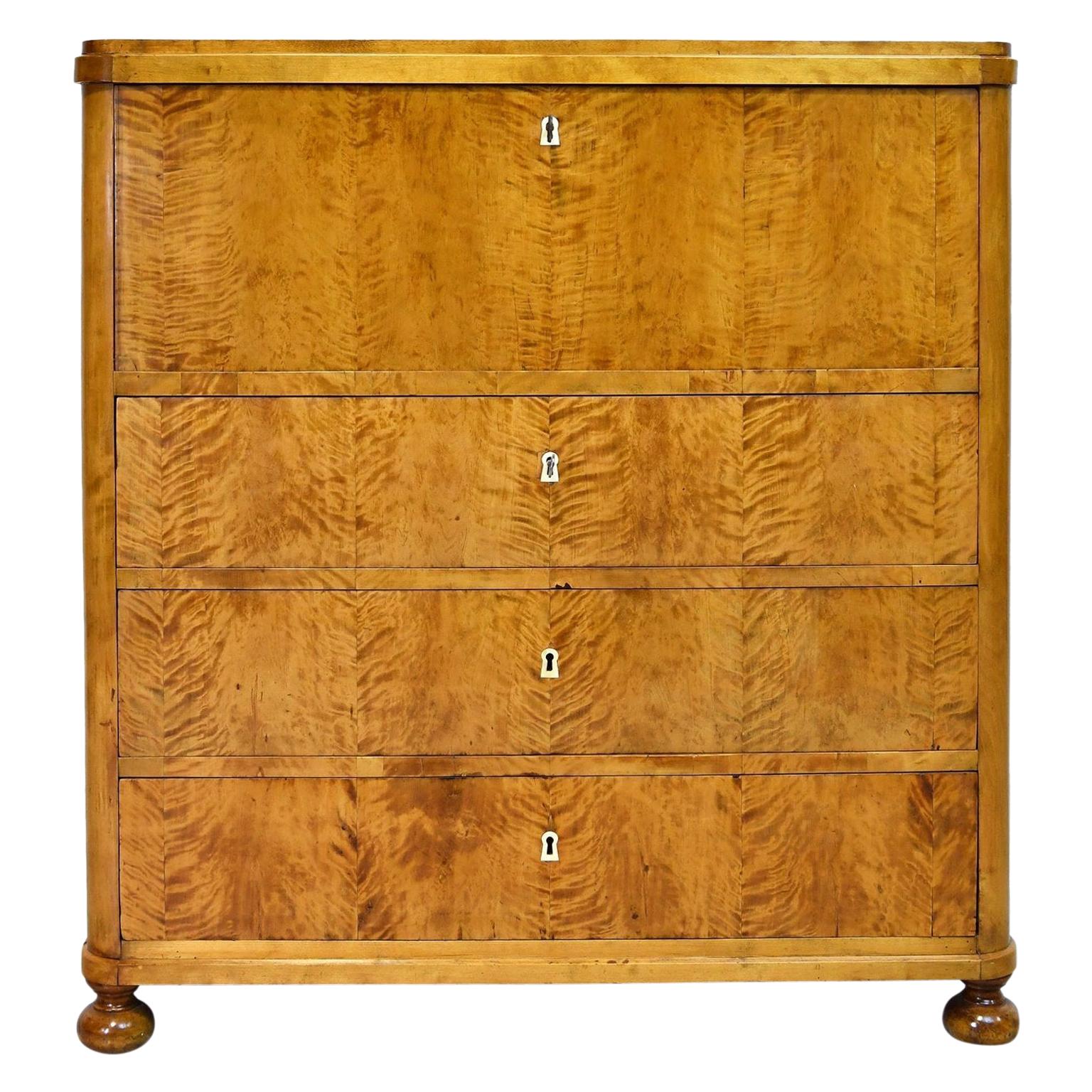 Swedish Karl Johan Biedermeier chest of drawers in book-matched fire birch veneer with fall-front secretary opening to reveal seventeen small drawers and a central cubby whose fascia are all in burled olive wood with turned pulls. Nine interior