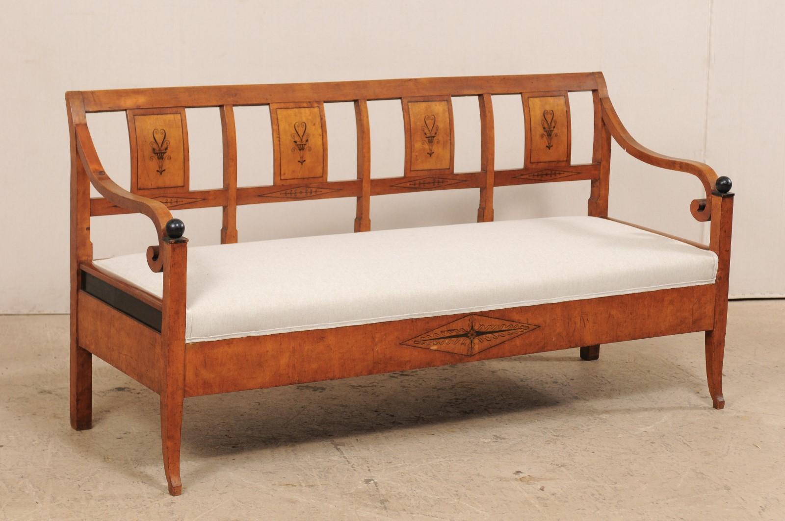 A Swedish Karl Johan sofa bench with upholstered seat from the mid-19th century. This antique settee from Sweden features an open back with wooden back rests, nicely decorated with floral and urn ebony colored acccents, framed within widely spaced