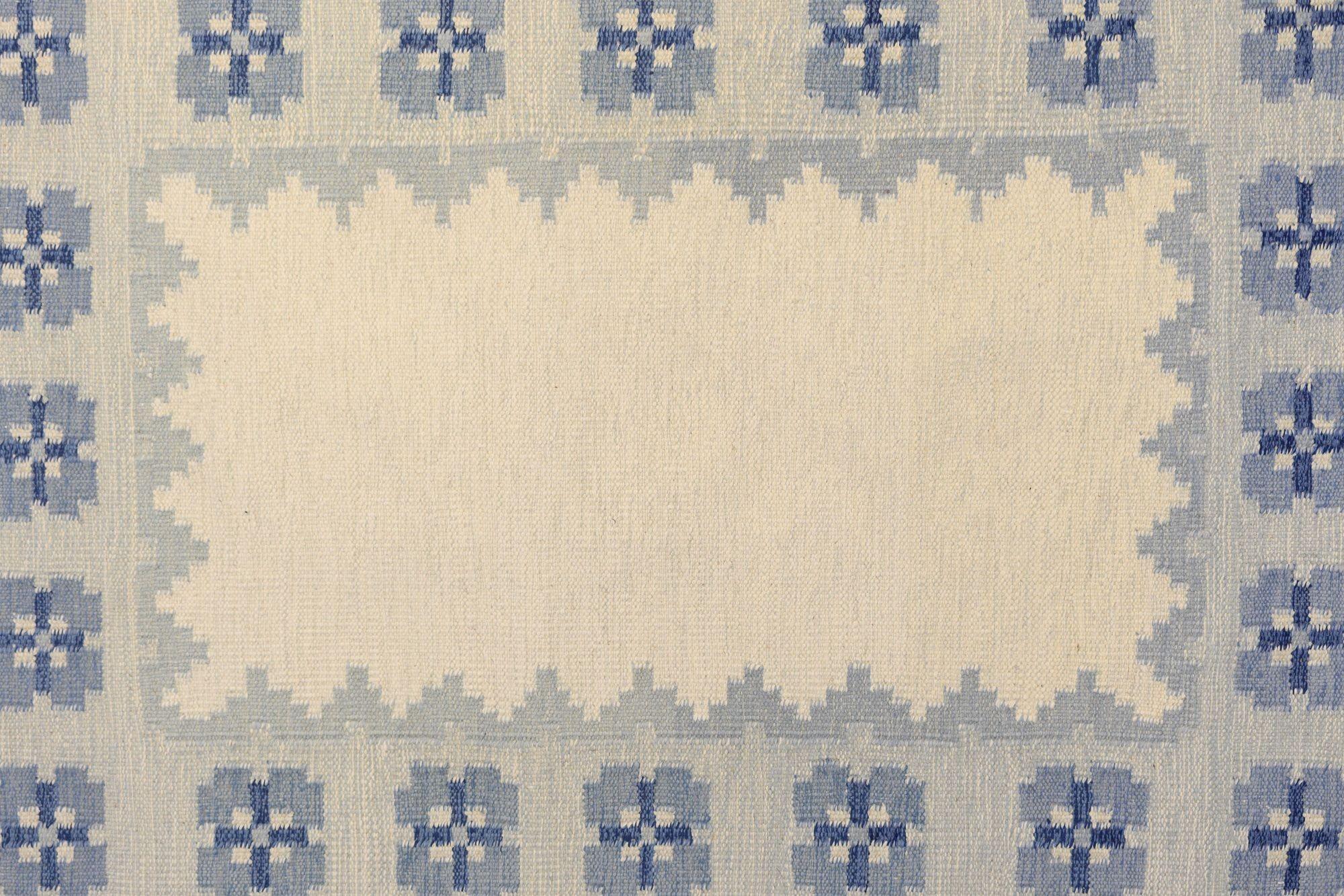 Swedish mid-century kilim in tones of blue and cream in a repeating floral pattern around the boarder leaving the central field clear. Signed E. Sweden circa 1960. All our carpets undergo a professional cleaning process. However, due to their age