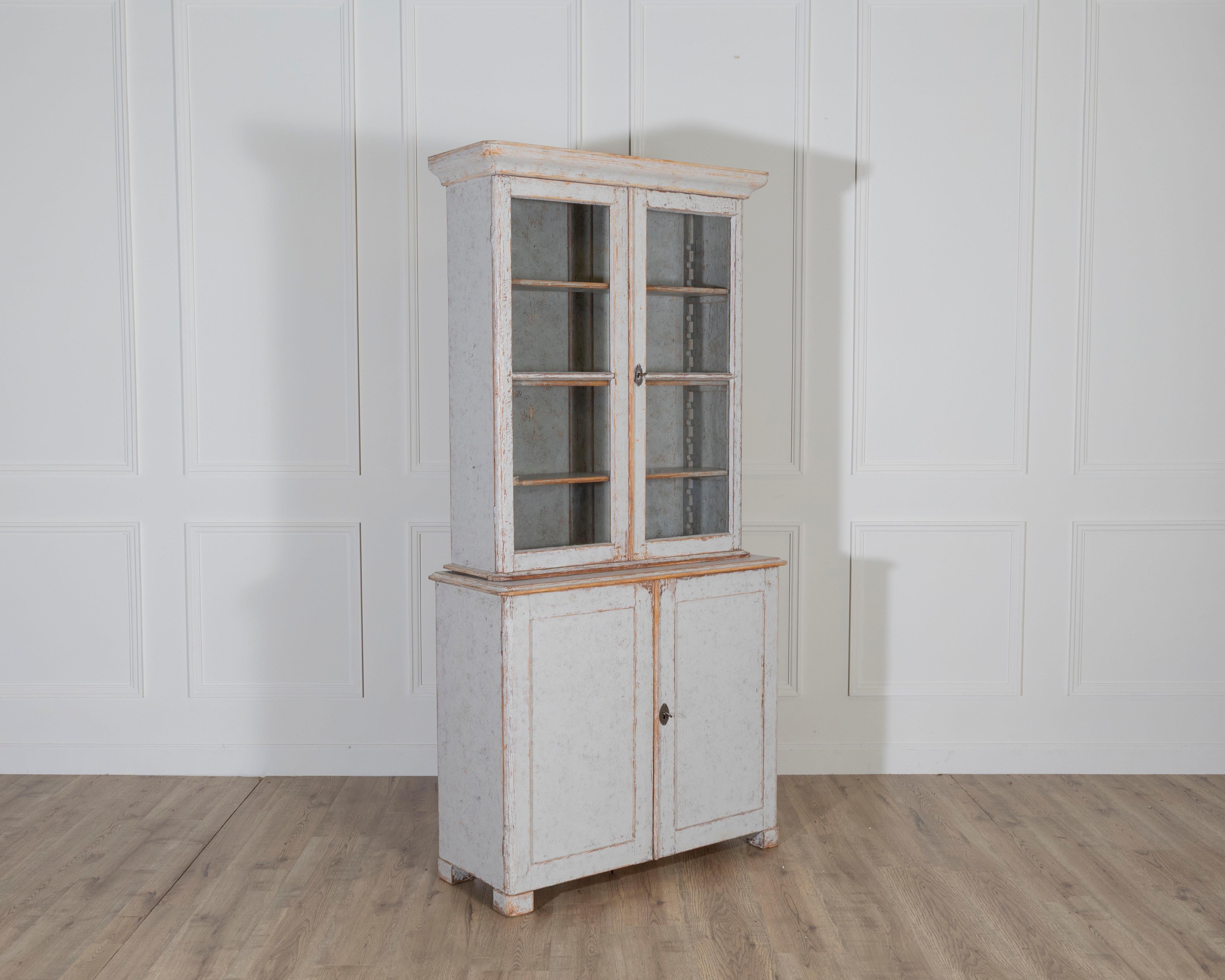 A charming Swedish bookcase from the late 19th century, newly repainted in a soft grey on the exterior with a bluish-grey wash inside. The upper section features a pair of glazed doors framed with mullions, opening to adjustable shelving ideal for