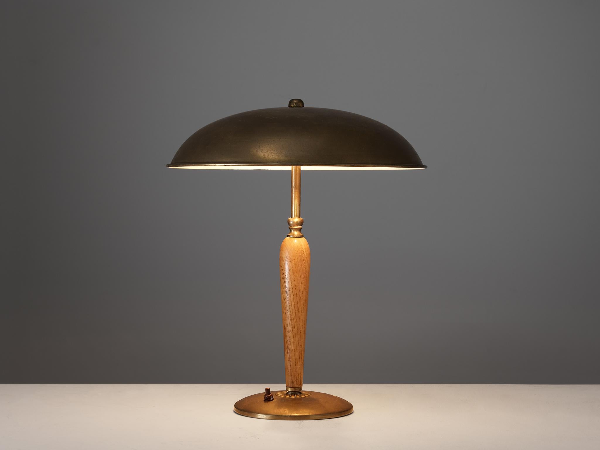 Desk / table lamp, brass, oak, Sweden, 1940s.

This exquisite table lamp of Swedish origin undoubtedly breathes the late Art Deco Period of the 1940s. The shade is executed in a semicircular shape with a white lacquered interior which creates a a