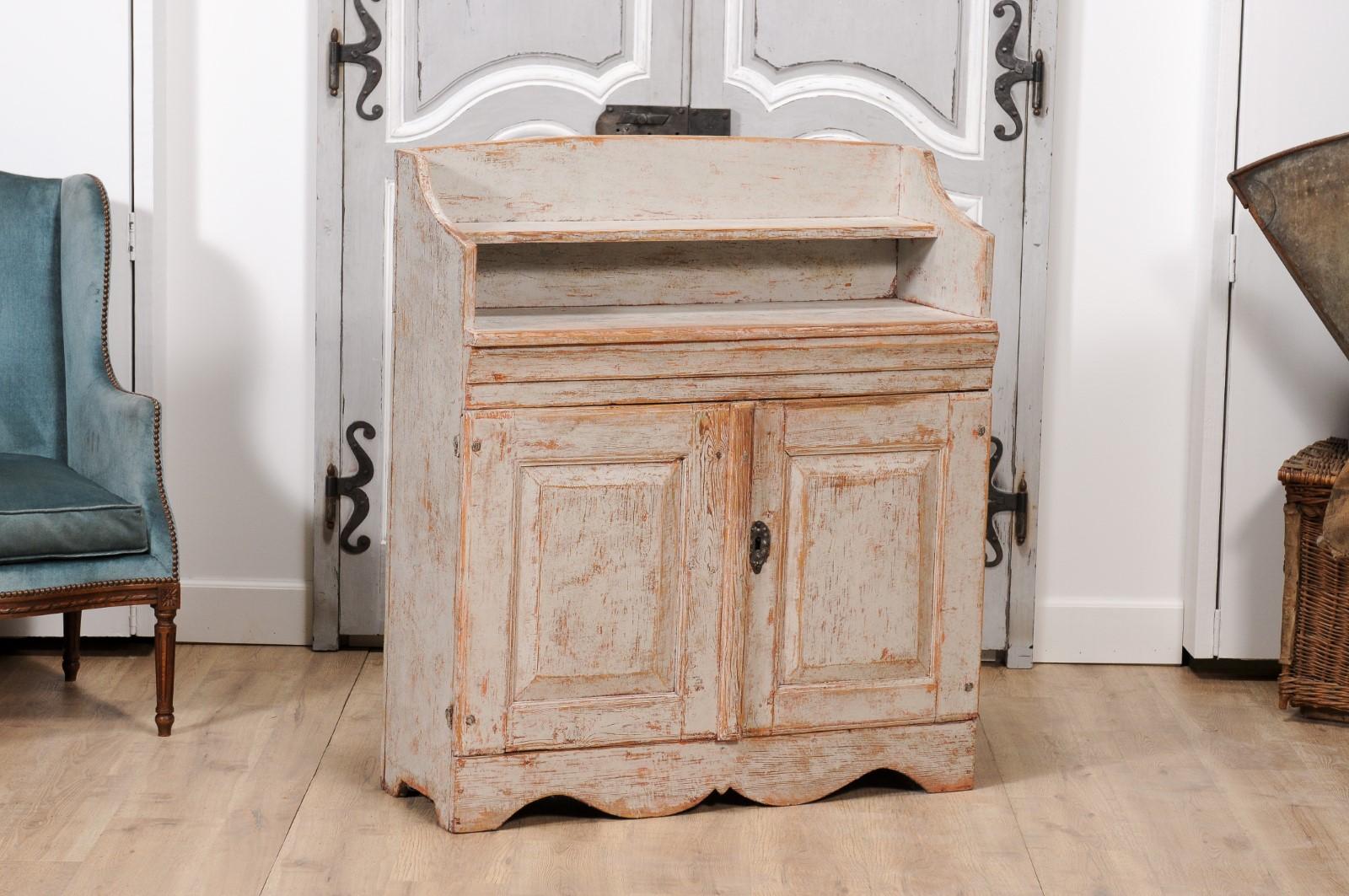 A Swedish late Gustavian period painted wood buffet from circa 1820 with open shelf in the upper section, two doors below and scalloped plinth.  Emanating the refined charm of the late Gustavian period, this Swedish painted wood buffet from circa