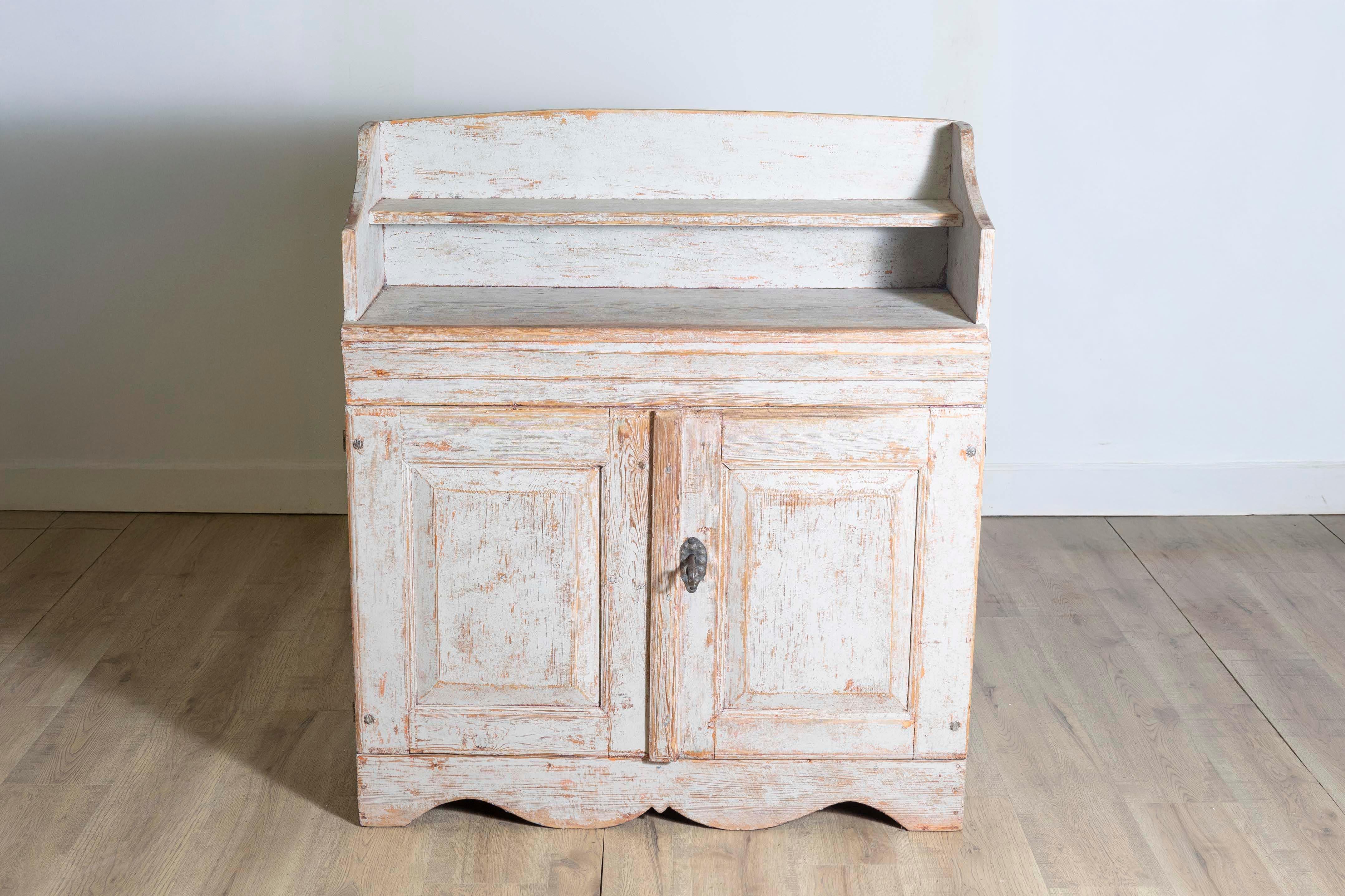 Bufé sueco de madera pintada de finales del periodo Gustaviano, de hacia 1820, con estante abierto en la parte superior, dos puertas debajo y zócalo festoneado.  Este bufé sueco de madera pintada de hacia 1820, que desprende el refinado encanto de