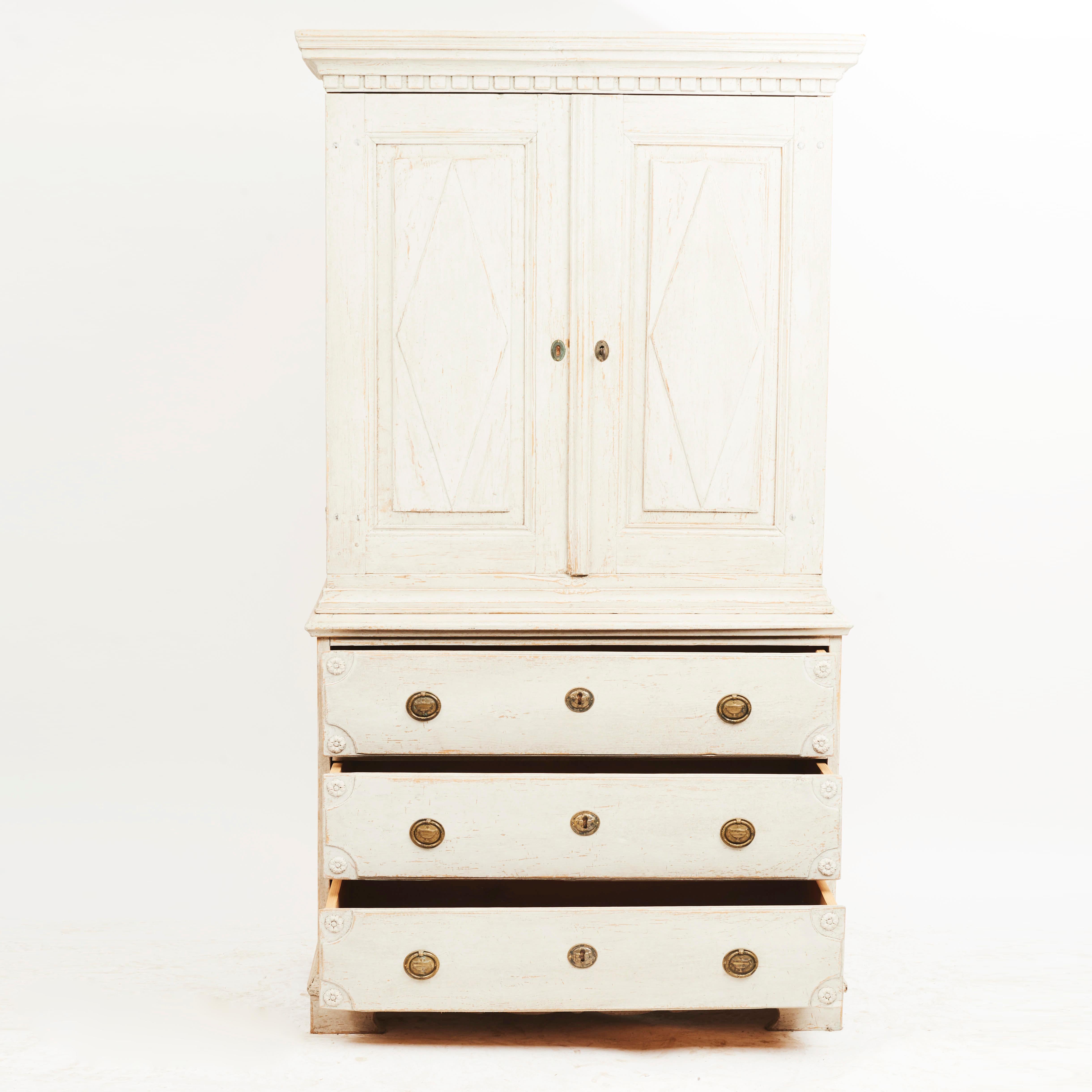 Swedish late Gustavian two-part linen press. Light grey painted pine wood.
Two doors in the upper cabinet with filling in the form of rhombuses. Cornice with dental frieze beneath. Three drawers below with floral motif carvings.
Sweden circa